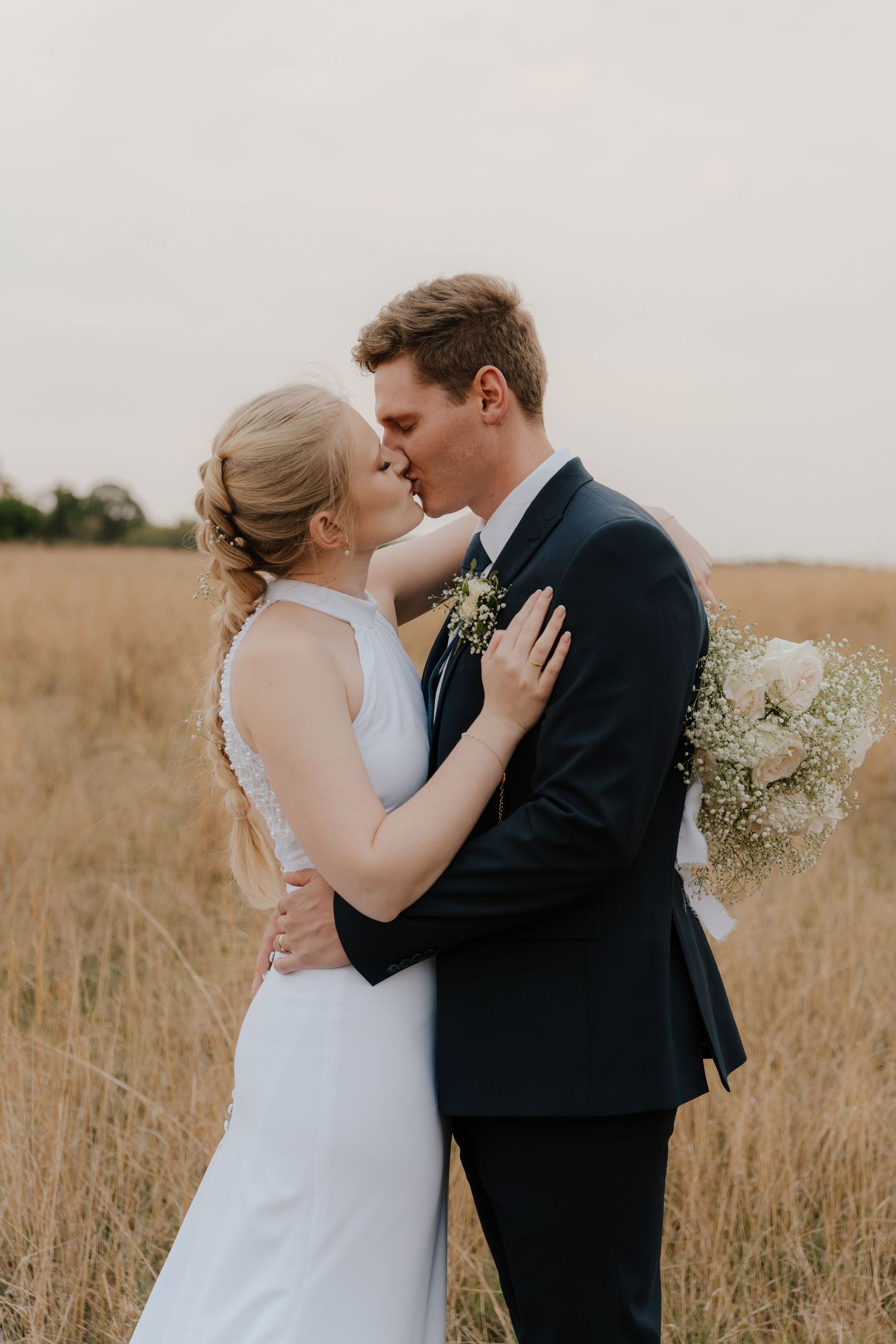 Romantic wedding couple sharing an intimate kiss in a golden wheat field at sunset.