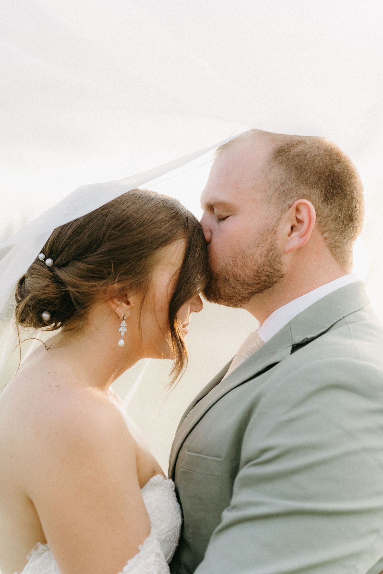 A tender wedding portrait showing a romantic moment between newlyweds against a bright background.