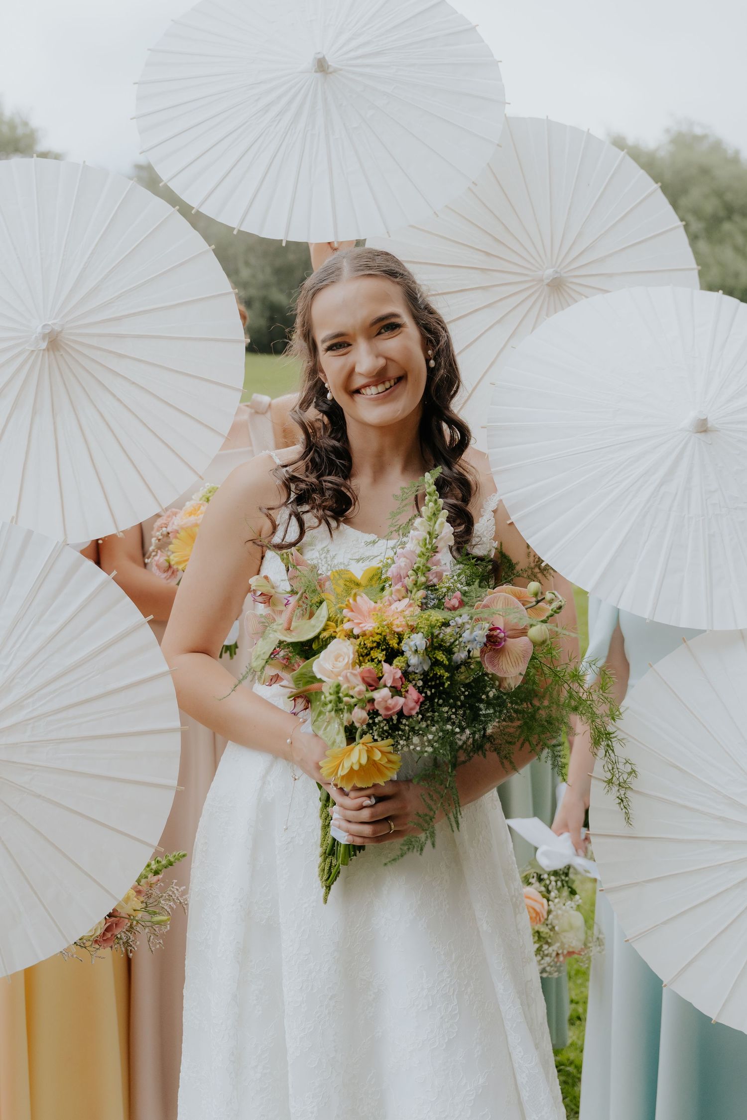 A beautiful spring wedding scene with white paper parasols and a colorful wildflower bouquet against a pastel backdrop.