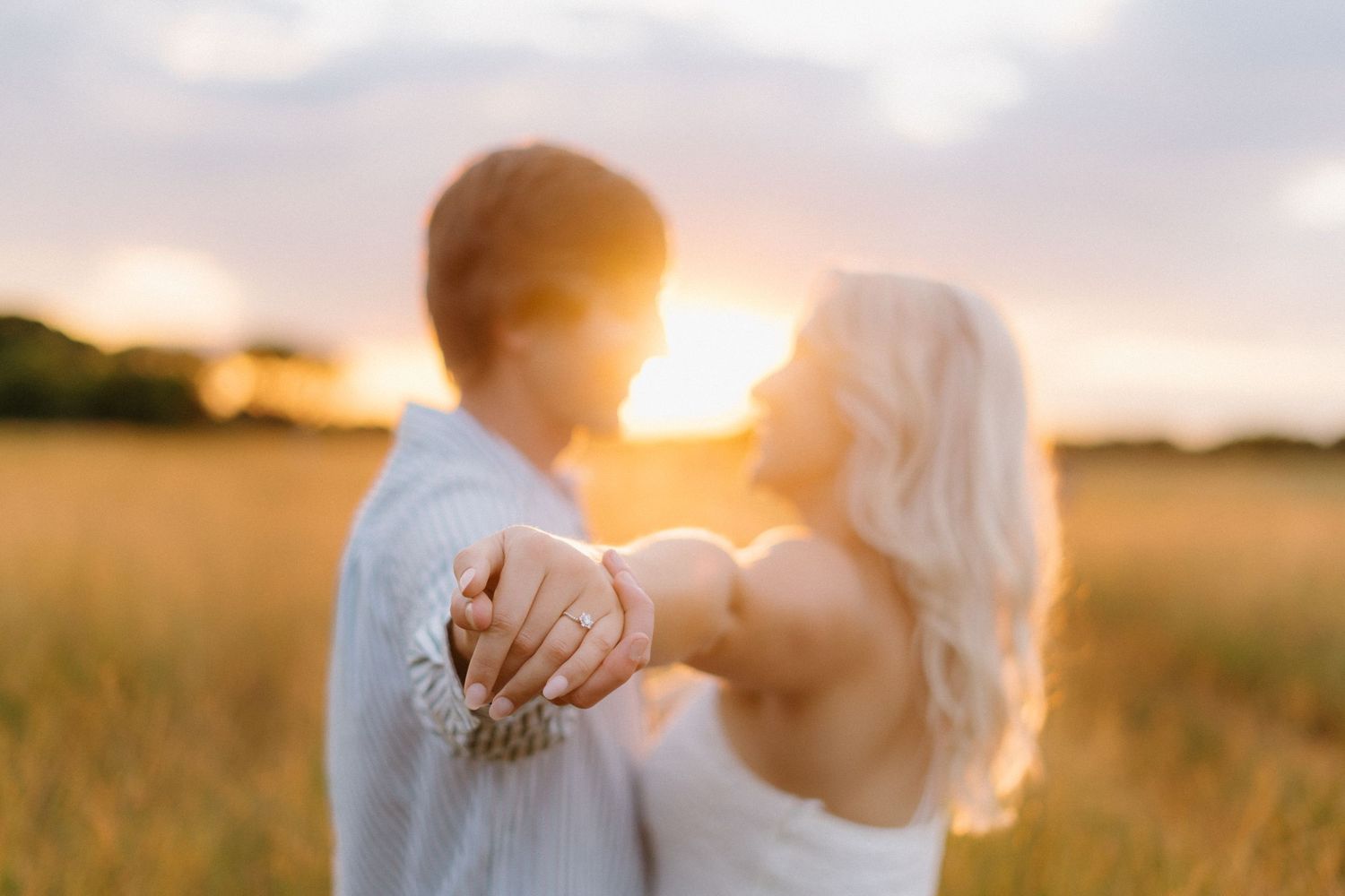 A romantic couple dances in a golden wheat field during sunset, creating a dreamy silhouette against the warm sky.