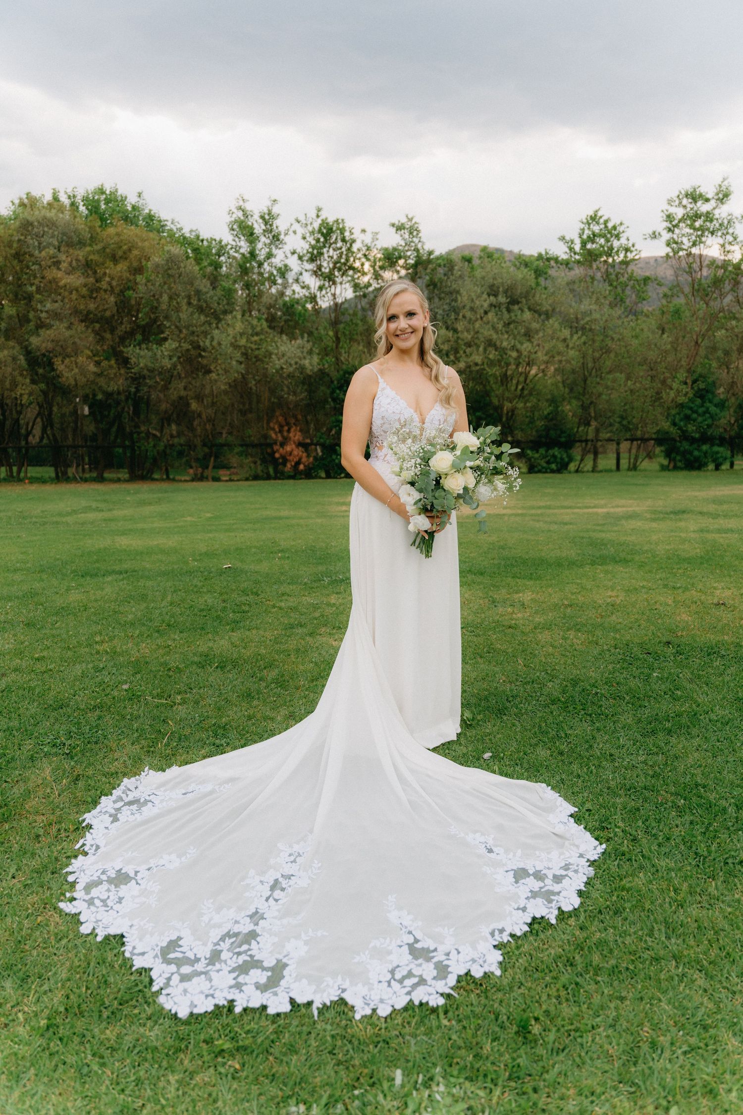 Elegant white wedding dress with intricate lace train displayed on green grass.
