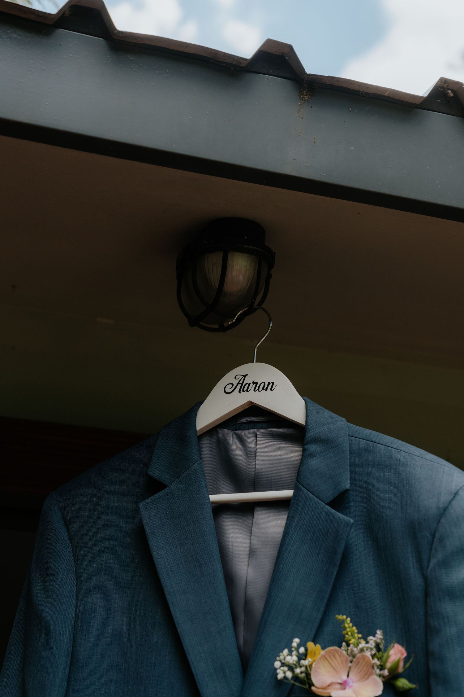 Row of navy blue groomsmen suits hanging on wooden hangers with delicate floral boutonnieres.