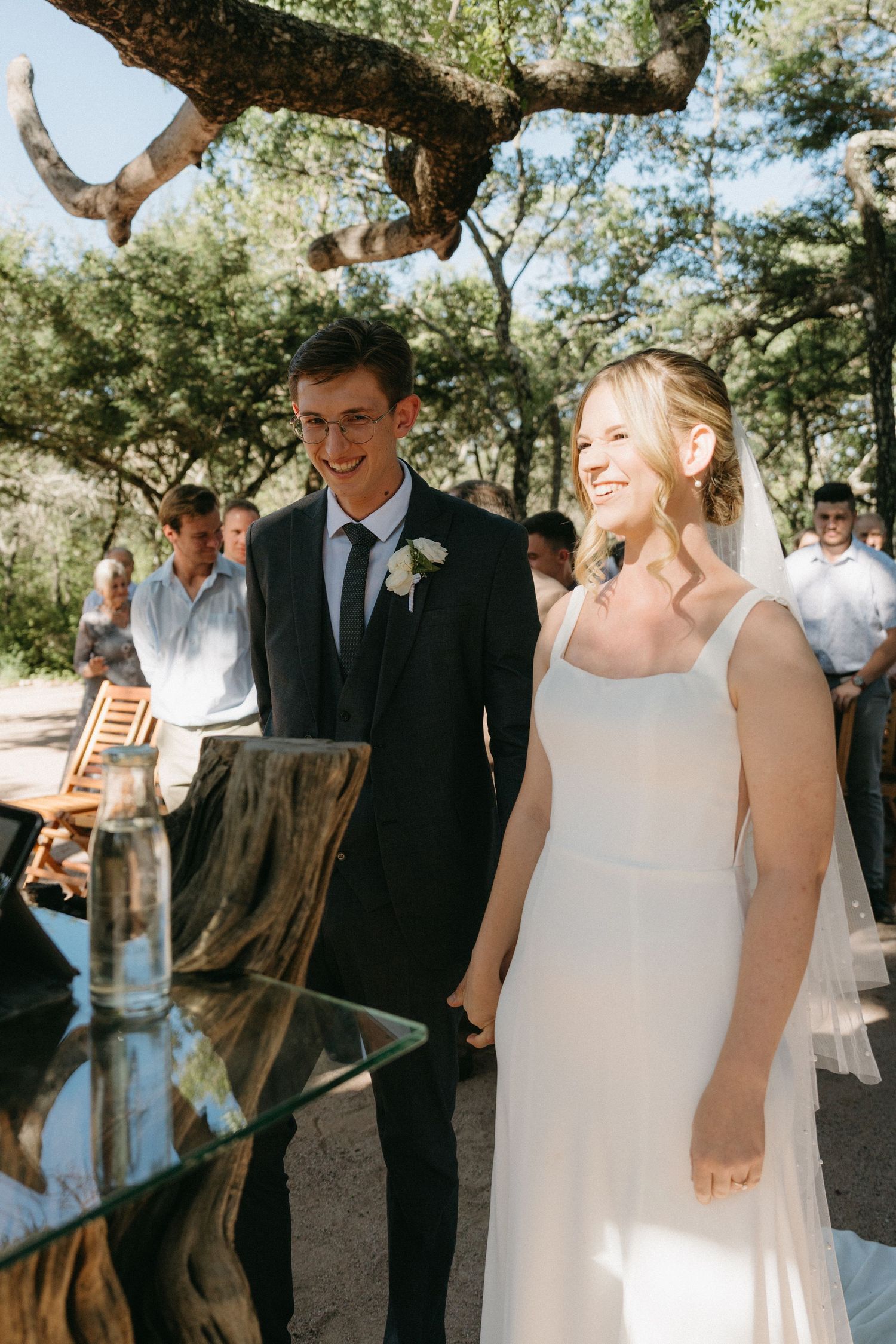 A joyful outdoor wedding ceremony with a couple standing at a rustic wooden altar surrounded by trees.