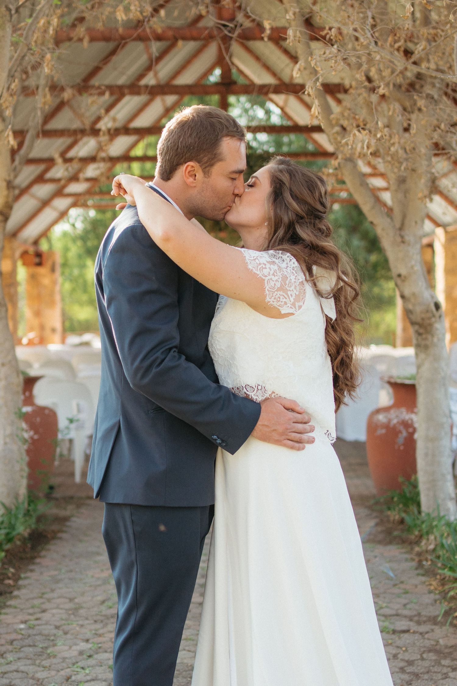 Romantic wedding couple sharing intimate kiss under rustic wooden archway.
