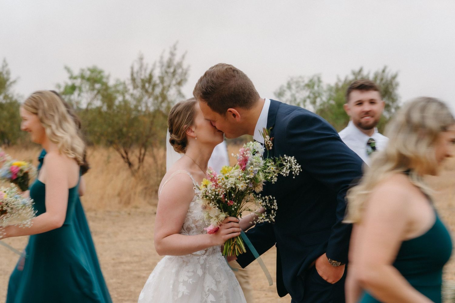 Tender wedding moment captured during outdoor ceremony with emerald-clad bridesmaids.