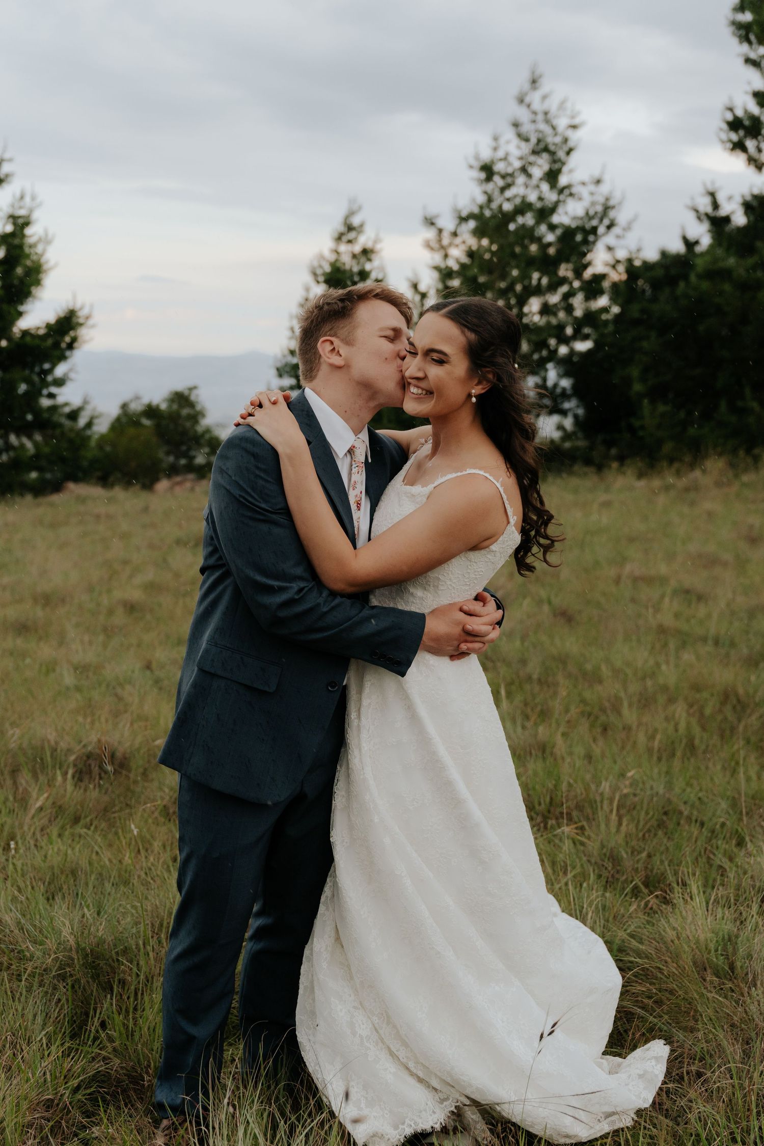 Newlywed couple shares romantic moments in a rustic outdoor field setting with natural lighting and tall grass.
