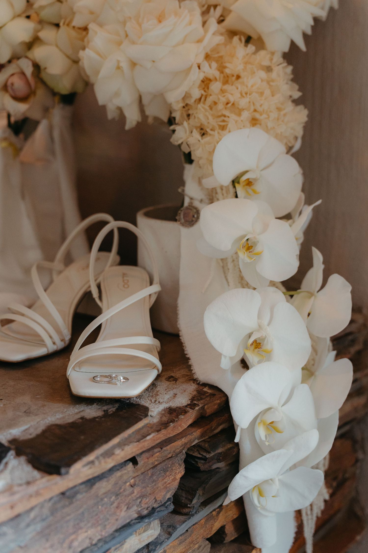 White orchid flowers arranged with delicate bridal shoes on a rustic wooden surface create an elegant wedding detail.