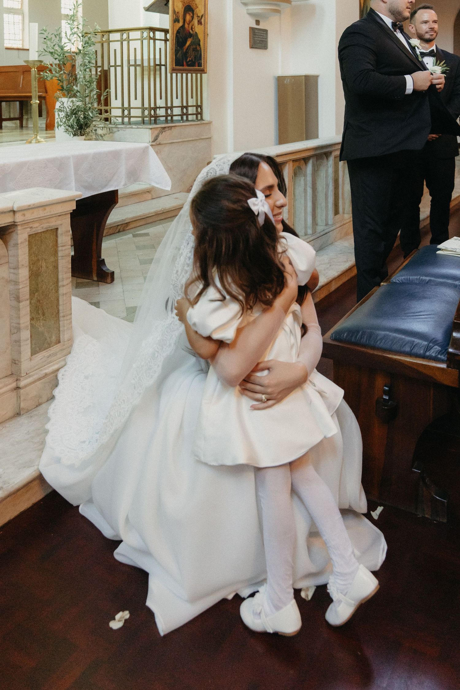 Bride in white gown hugging a flower girl in a church during a wedding ceremony at Rosebank Catholic Church