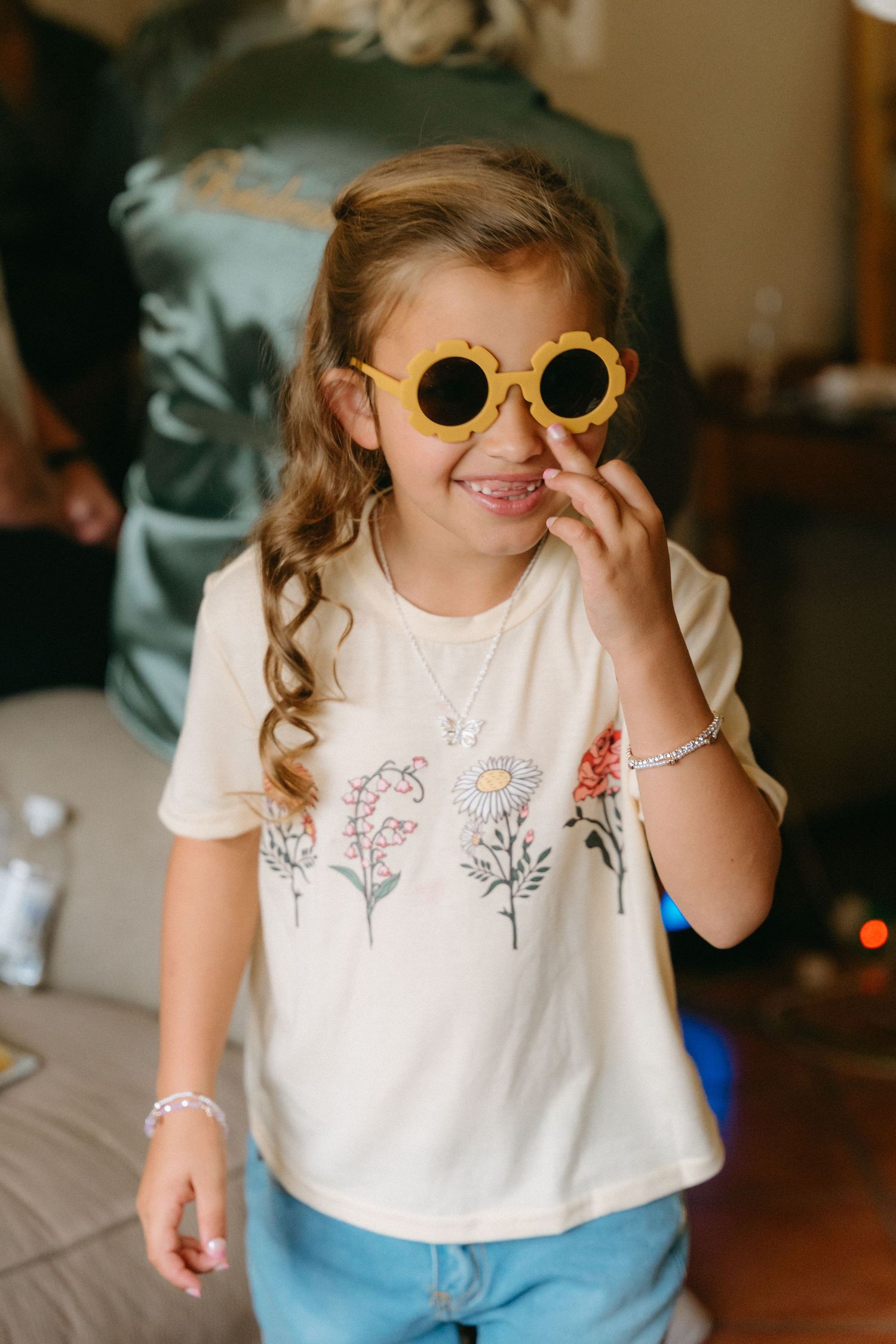 Young child wearing yellow sunglasses and floral t-shirt smiles playfully.