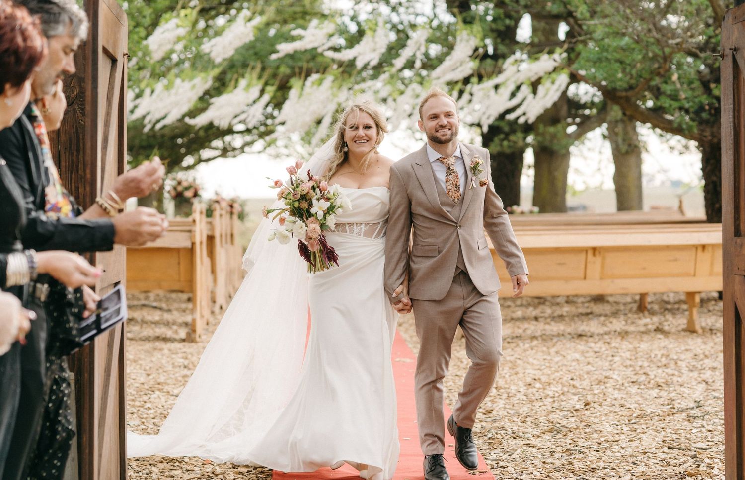A couple walks down the aisle at their outdoor wedding ceremony while guests celebrate.