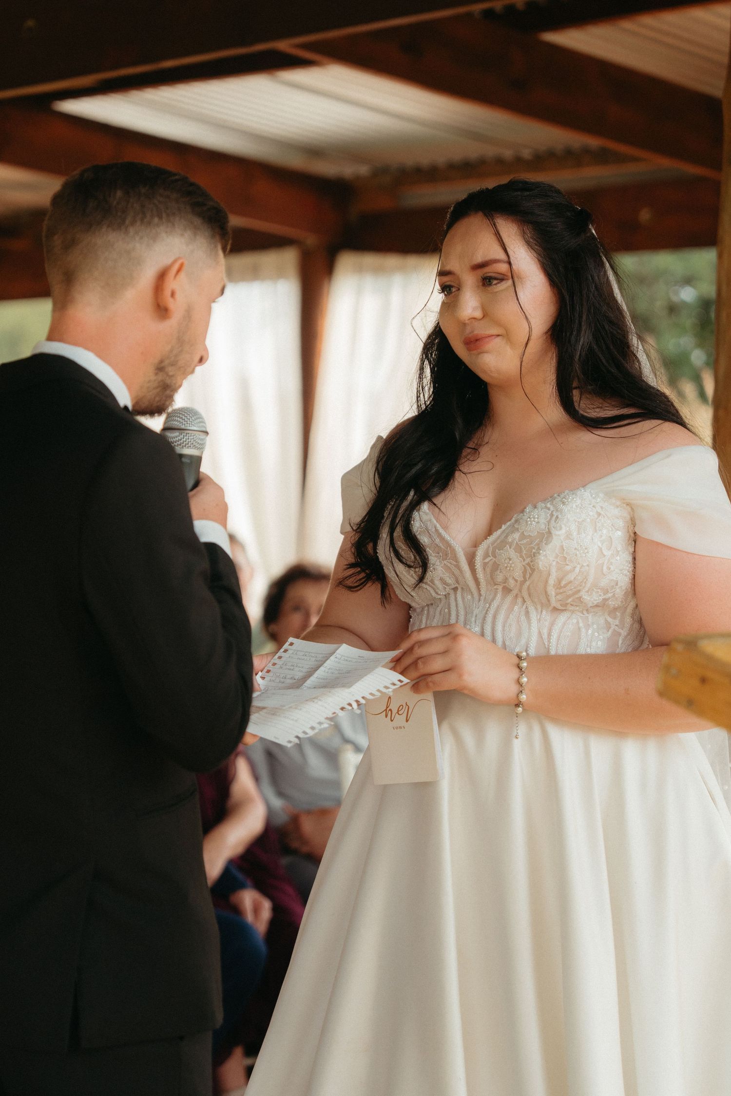 A couple exchanges wedding vows during an intimate indoor ceremony under wooden beams.