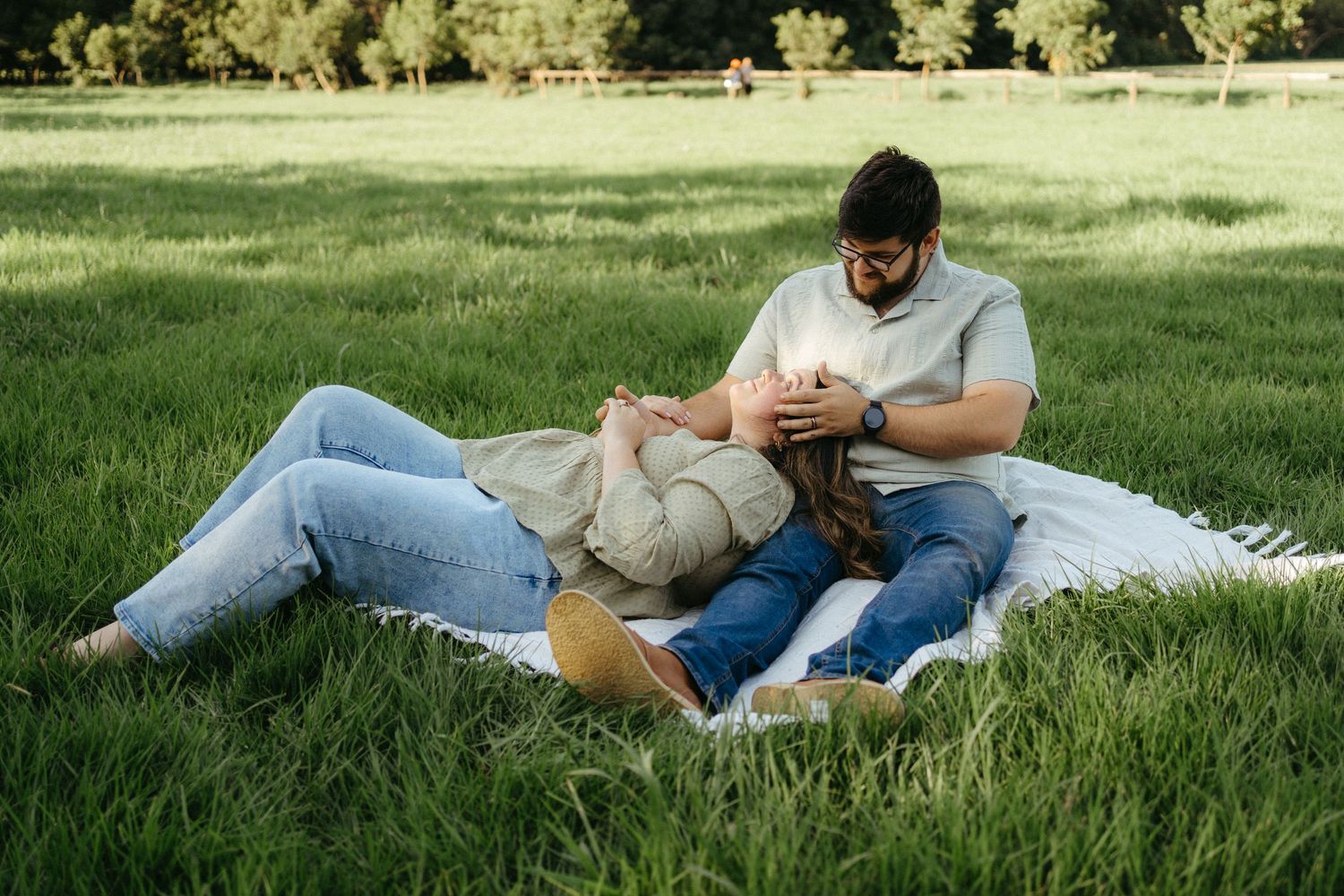 Couple relaxing together on blanket in sunny grass field while looking at mobile phone.