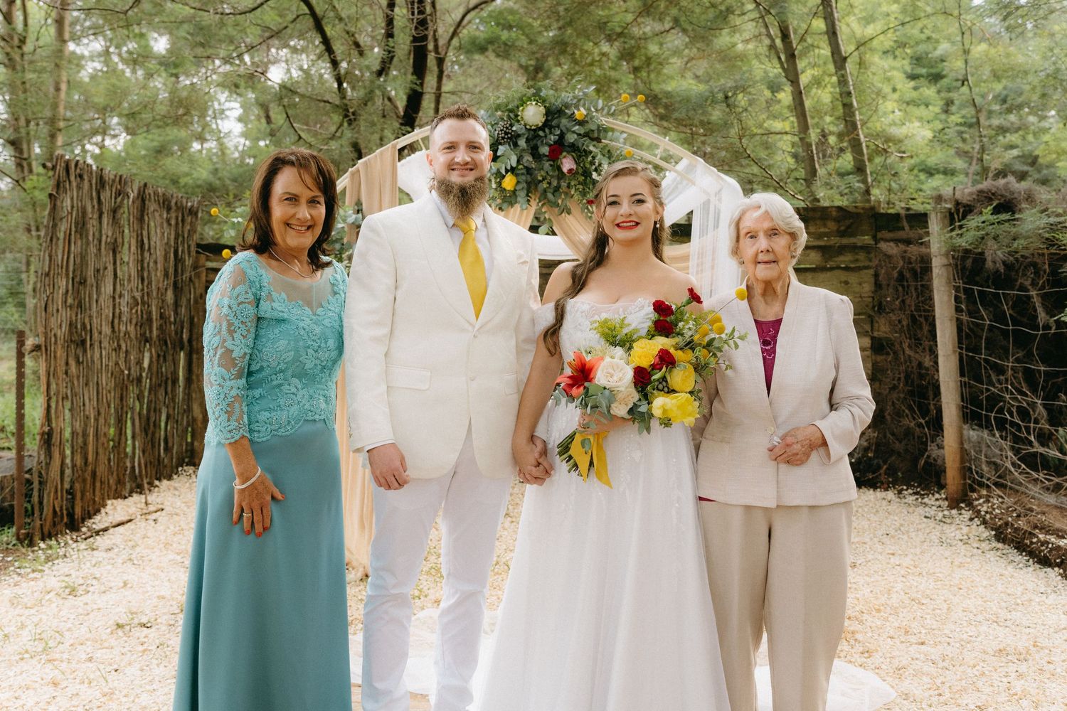 Wedding party in white, turquoise and yellow poses together on a wooded path.