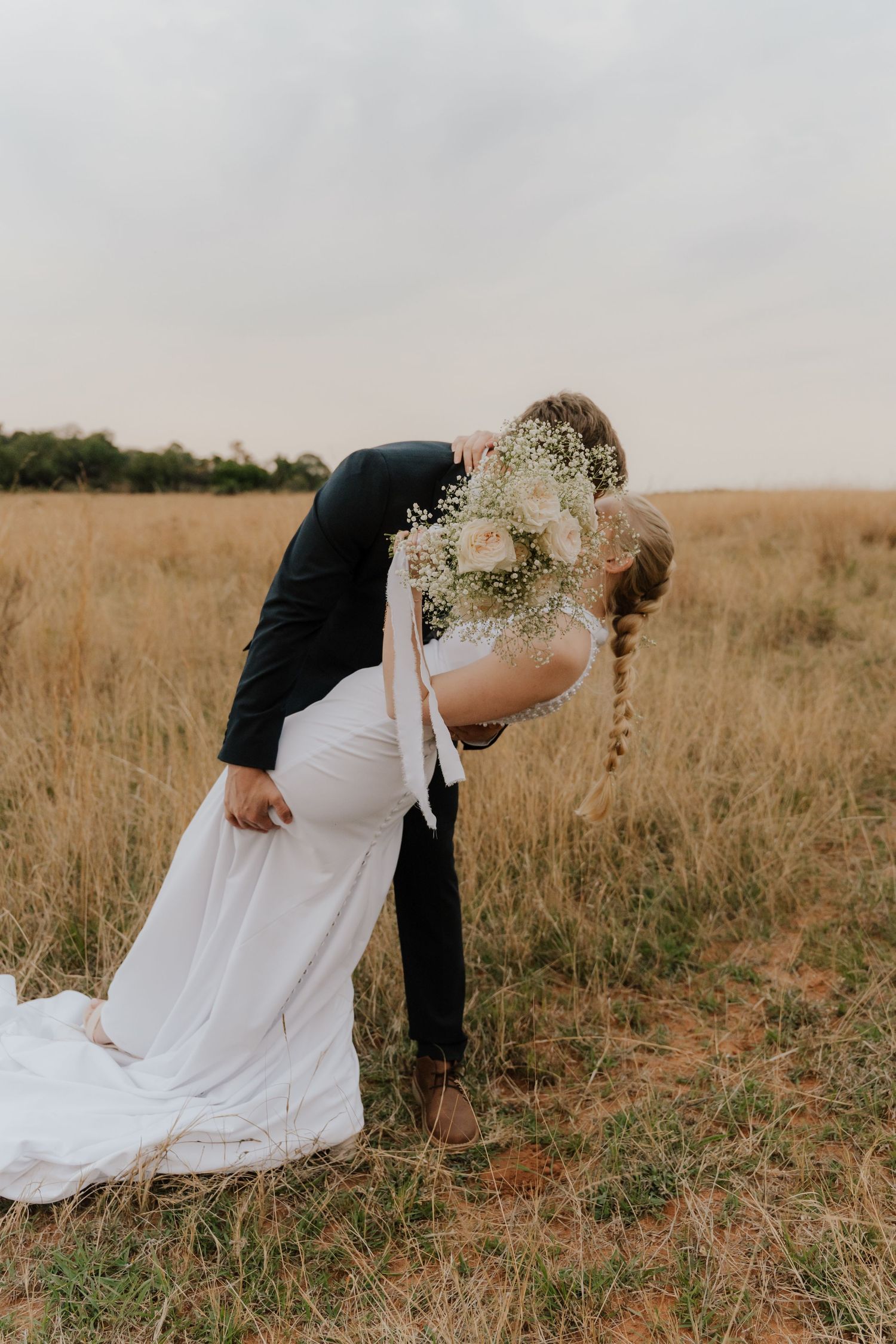 A romantic dip pose between a couple in formal attire against a golden field at sunset.