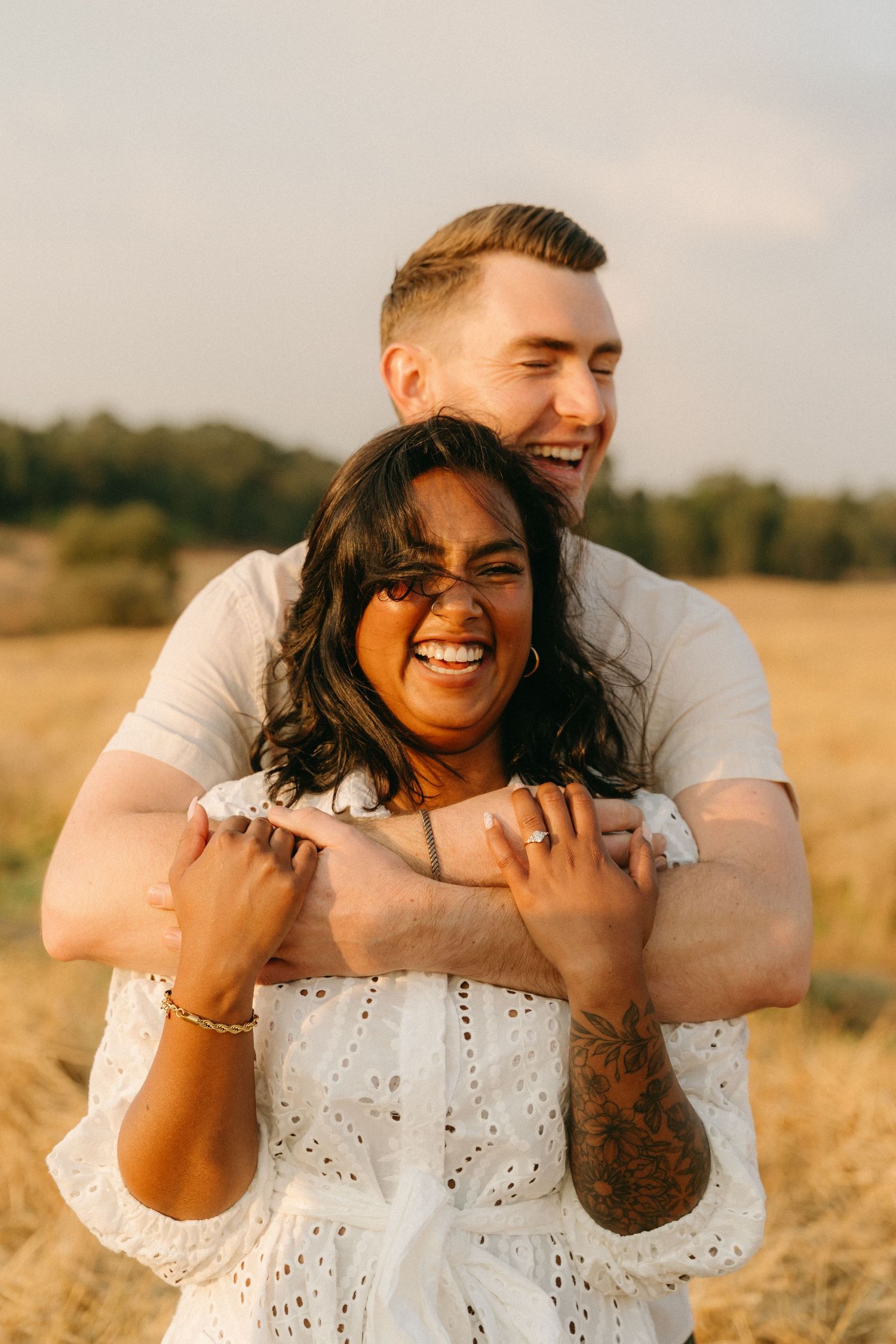 Couple laughing and embracing in a golden wheat field during sunset.