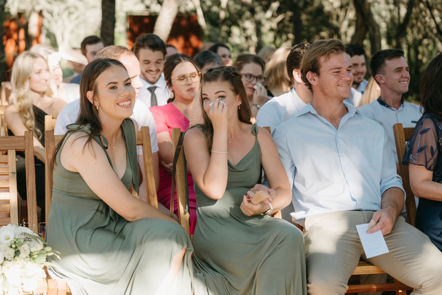 Wedding ceremony guests react with emotion while seated in outdoor chairs.