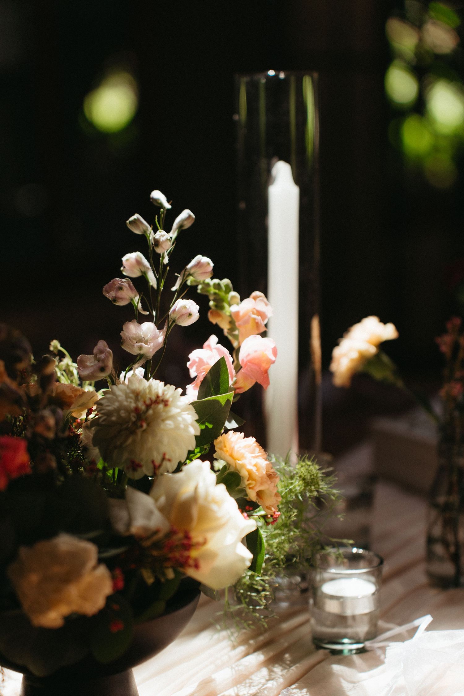 Elegant wedding table centerpiece with white and peach roses alongside a tall glass candle holder on white tablecloth.
