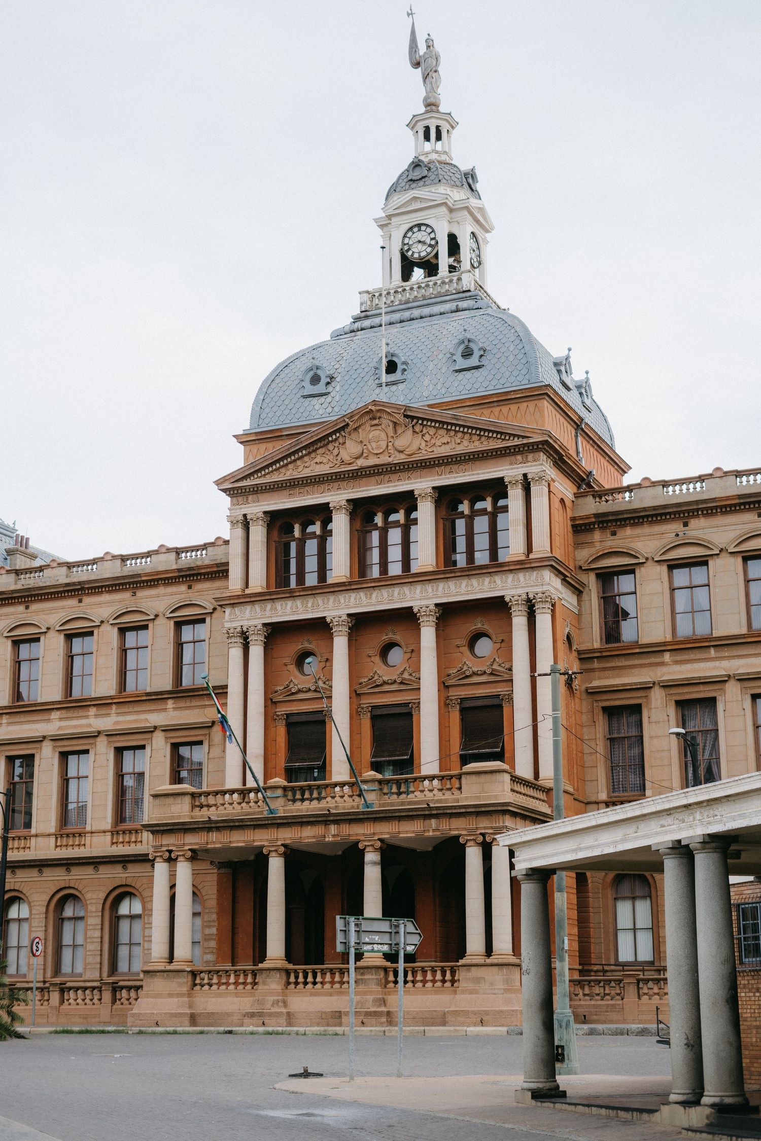 Historic government building with ornate architecture featuring a domed tower and classical columns in warm beige stone.