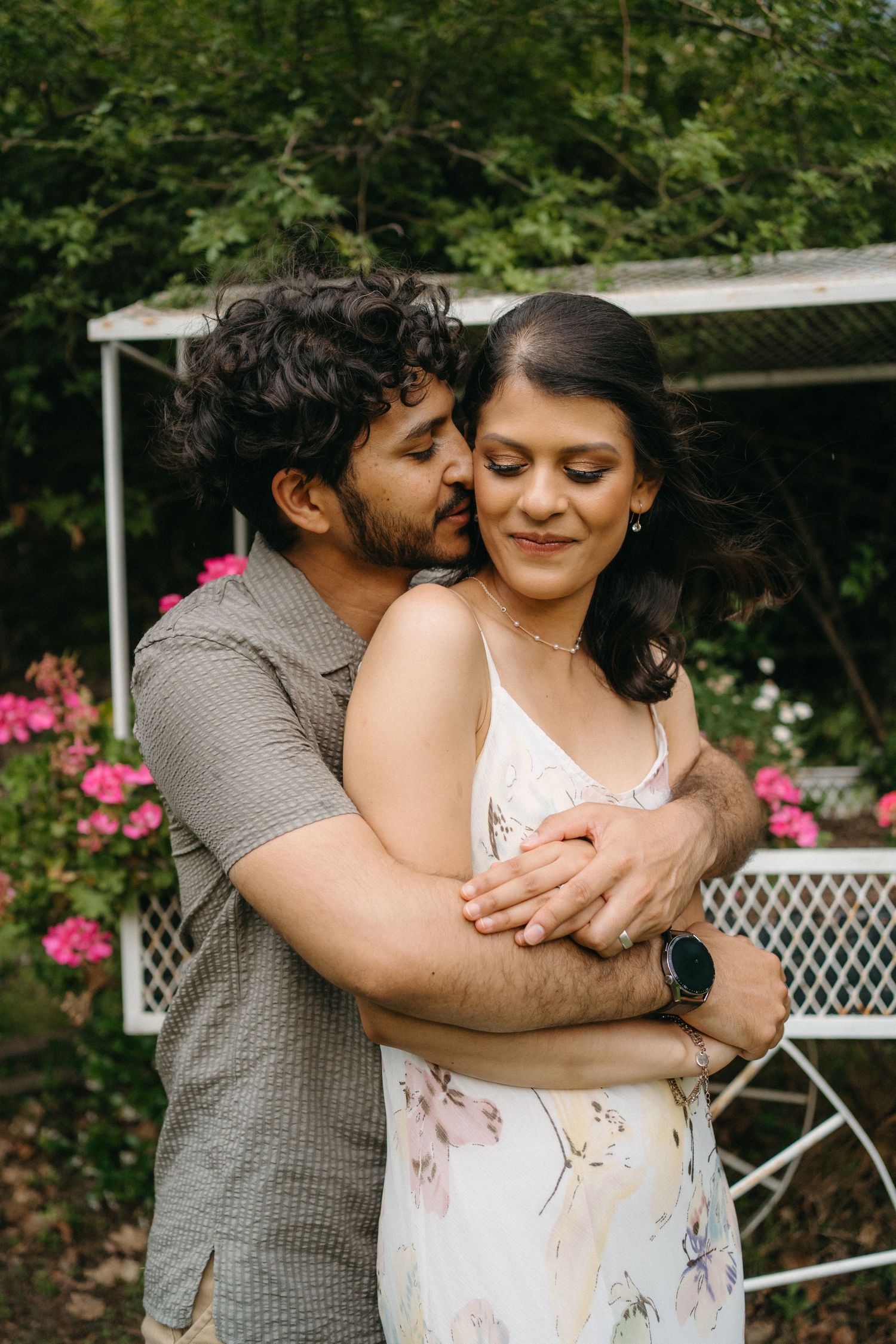 Tender moment between couple embracing in a garden setting with pink flowers.