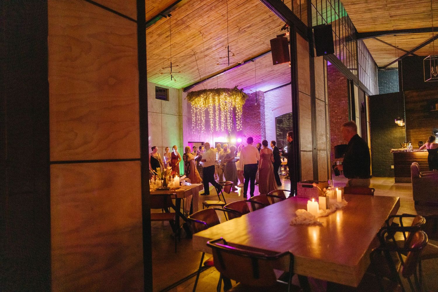 Wedding reception venue with purple lighting and wooden tables set up for dining.