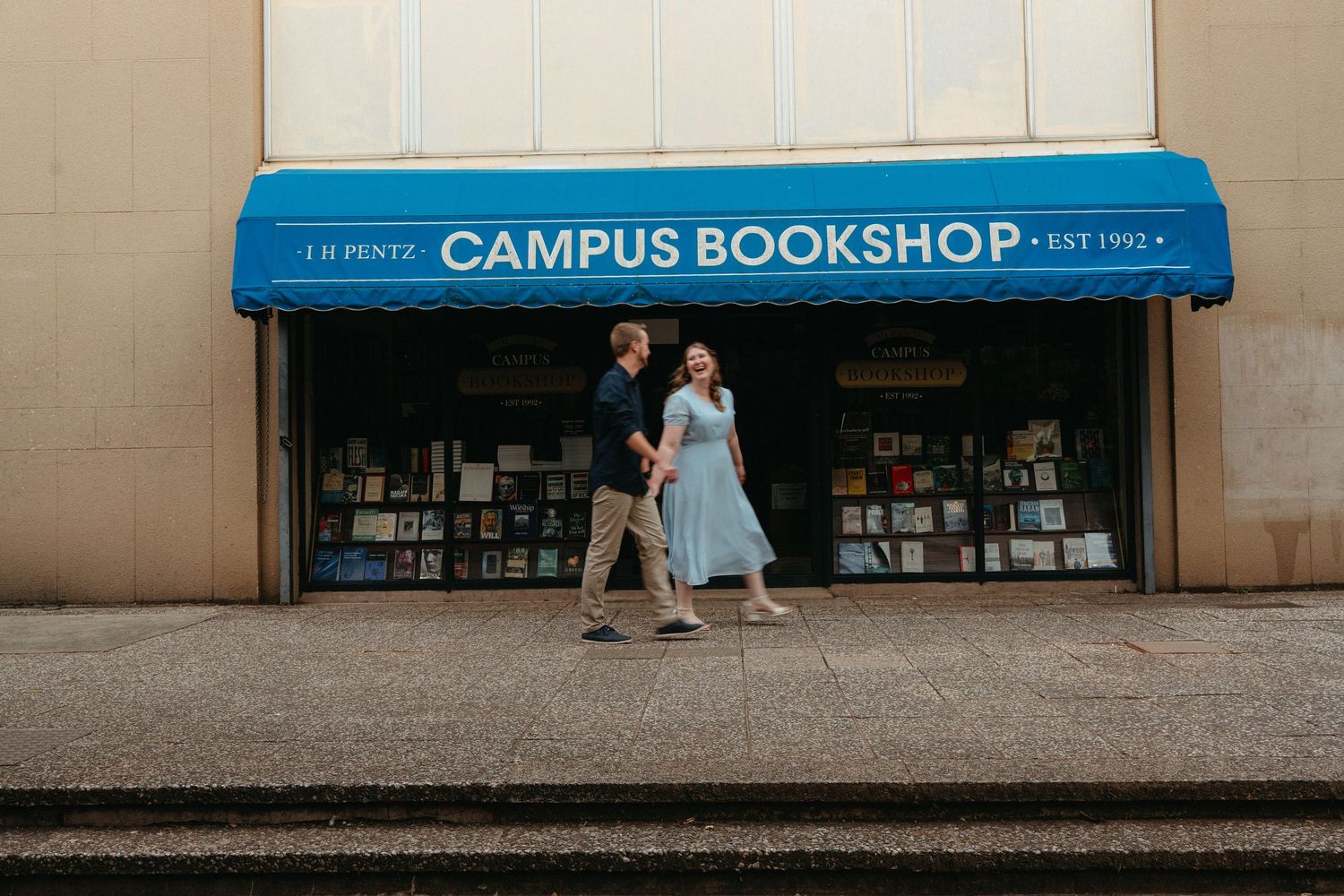 A blue campus bookshop storefront entrance with white lettering and steps leading to the door.
