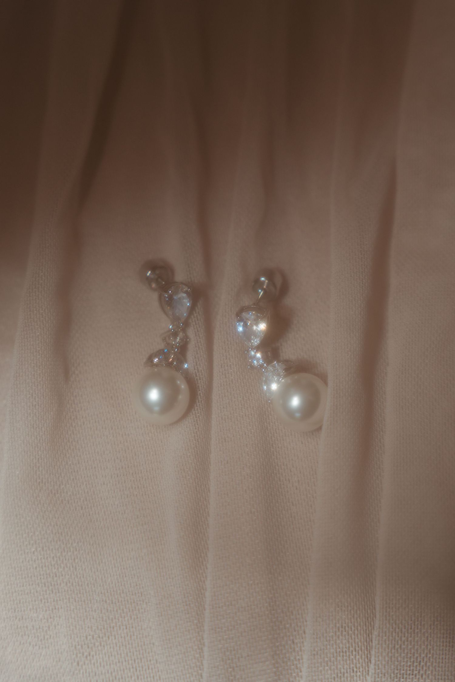 A close-up photo of delicate pearl stud earrings arranged in a row on a beige fabric background.