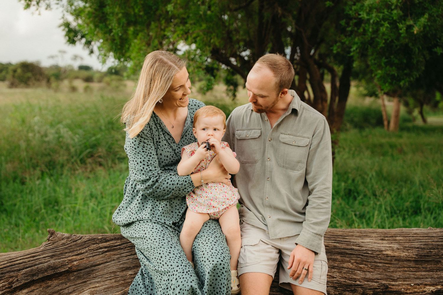 Young family with a baby sitting on a log in a lush green outdoor setting in Pretoria during a family photo session.