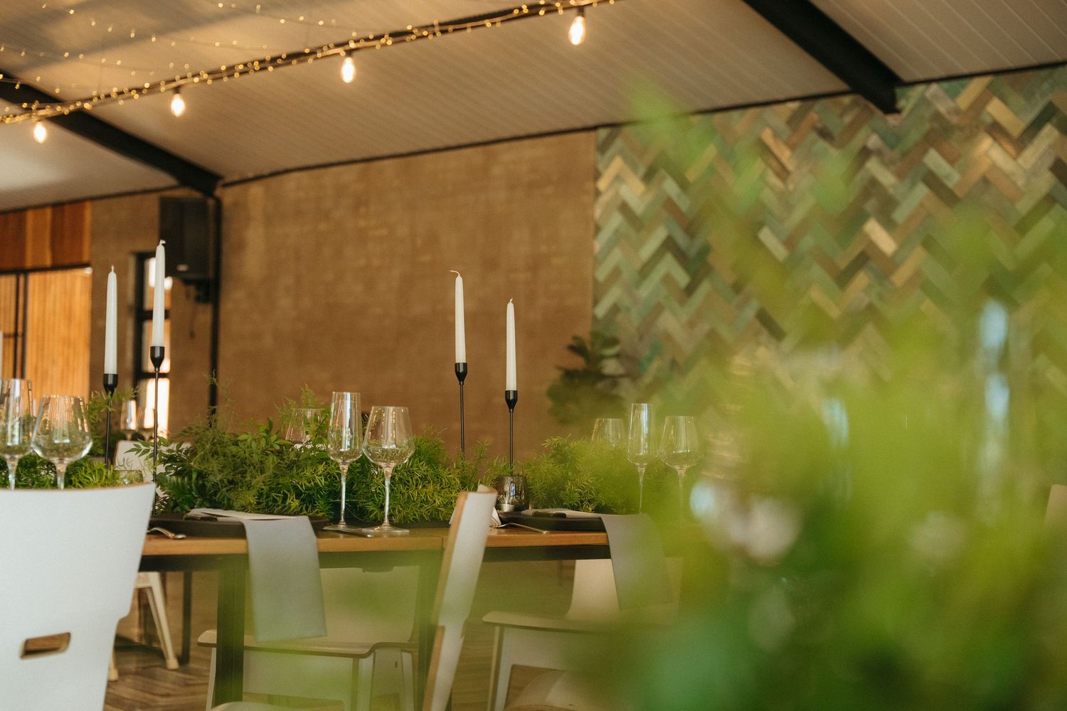 Elegant dining setup with candlesticks, wine glasses, and lush greenery under string lights.