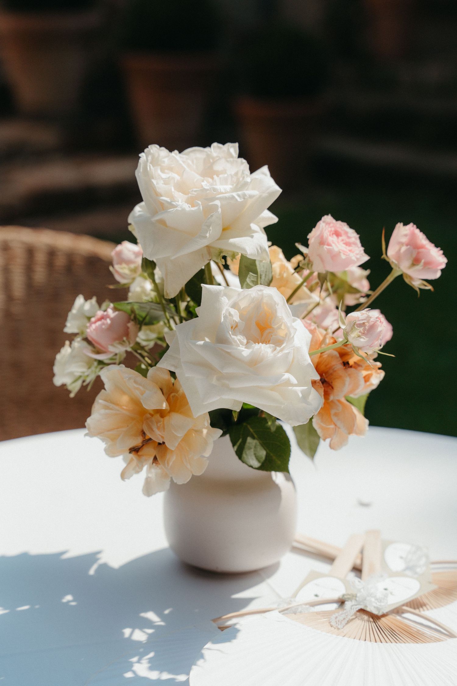 Elegant white and pink rose bouquet in a ceramic vase on a white table, bathed in warm sunlight outdoors.