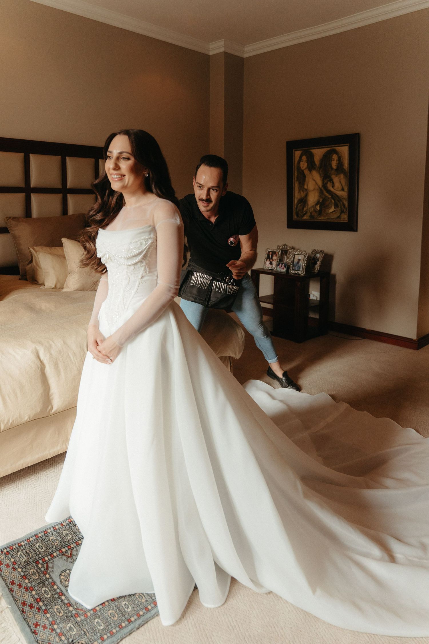 Bride in elegant white gown with long train smiles as Johannesburg photographer captures her wedding day preparations in a hotel room.