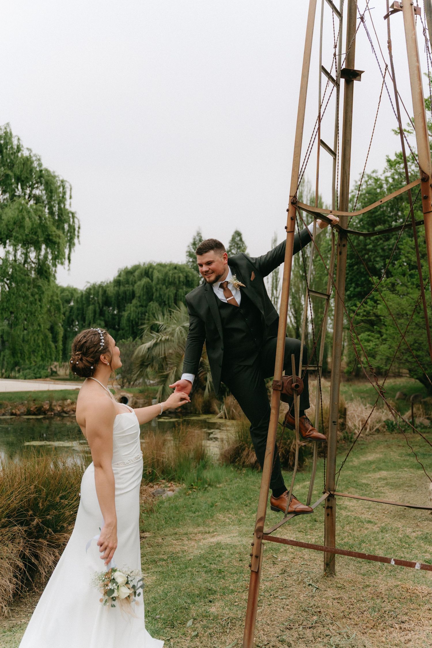 Newlyweds share playful moments together in an outdoor setting with wooden poles and greenery.