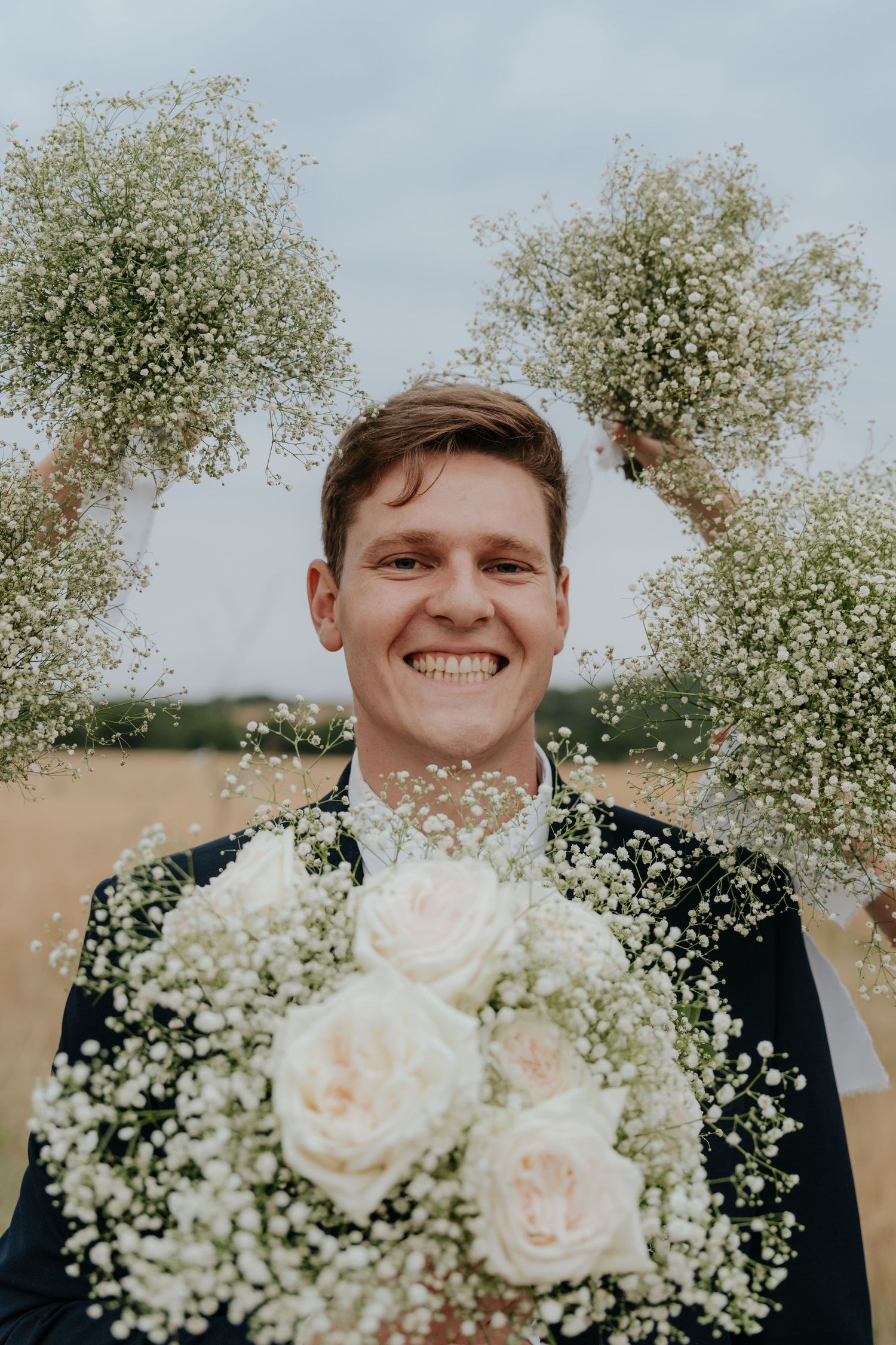 Wedding bouquet with white roses and baby's breath flowers against a cloudy sky.