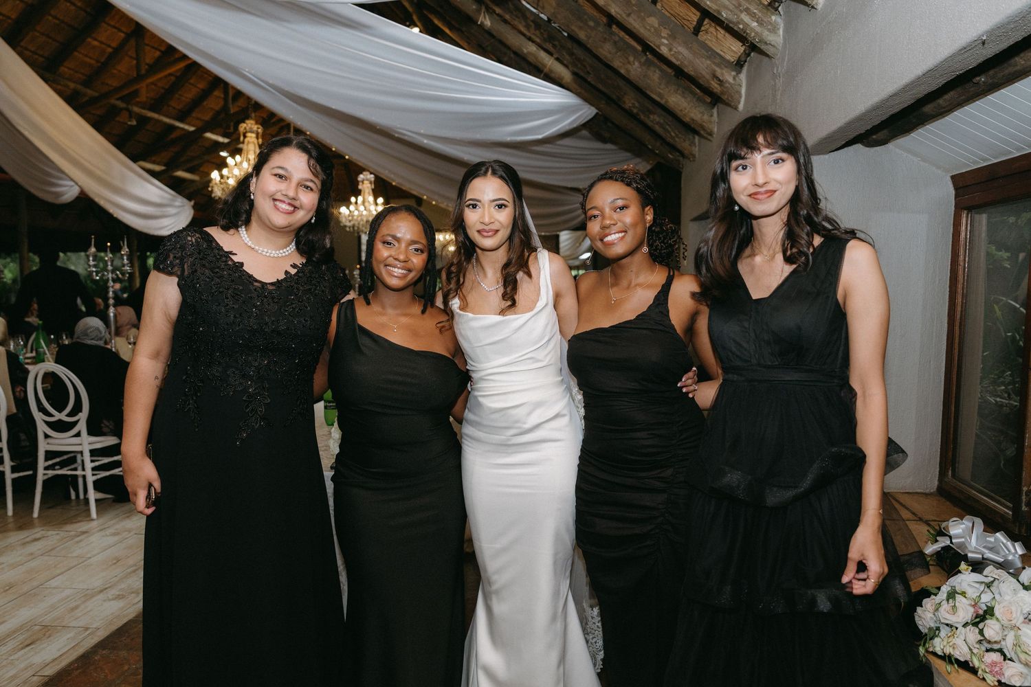 Wedding party in elegant black and white dresses pose together at reception venue.