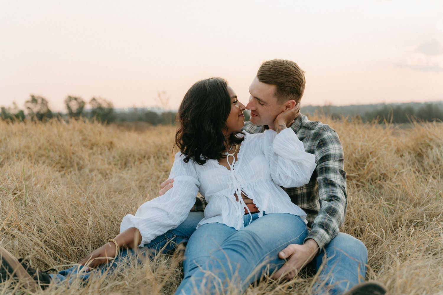 Couple relaxes together on blanket in rustic field during casual outdoor photoshoot wearing denim and plaid.