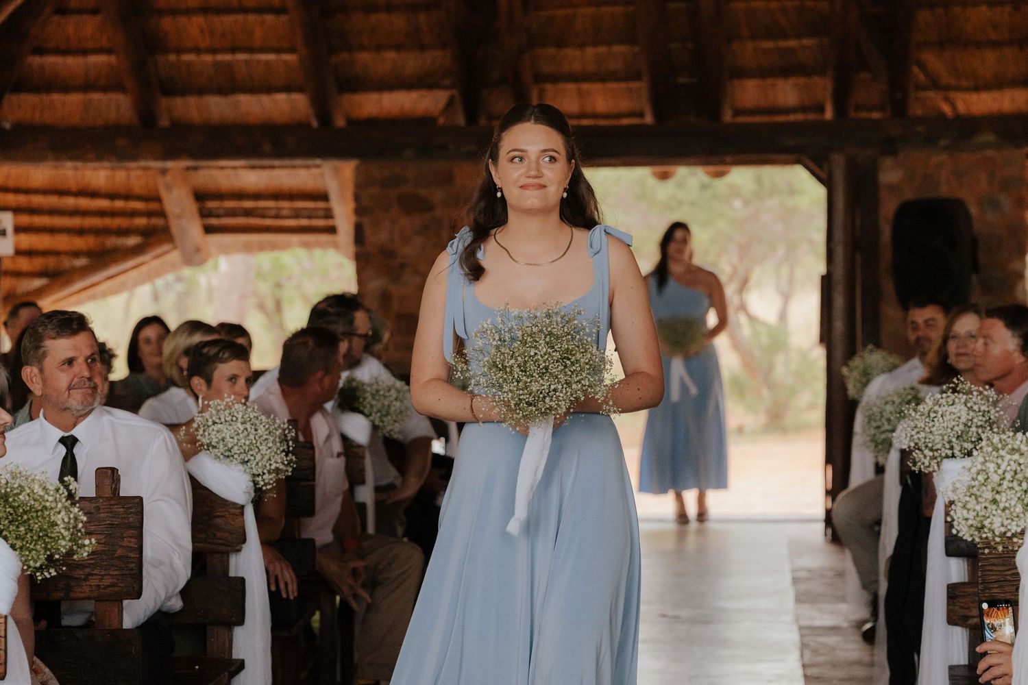 Wedding ceremony taking place in a rustic wooden pavilion with guests seated on benches.