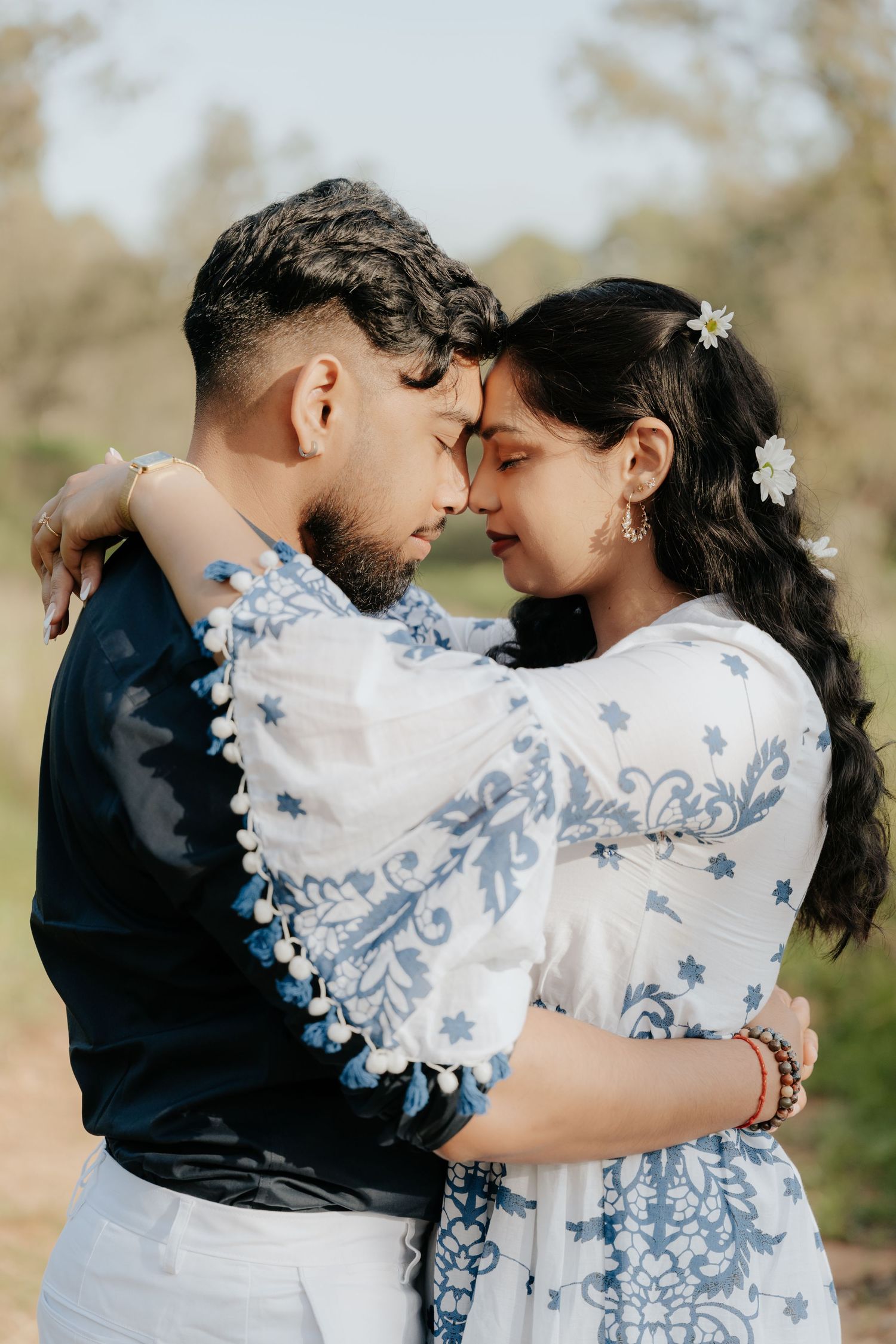 A romantic embrace between a couple wearing coordinated blue and white outfits in a dreamy outdoor setting.