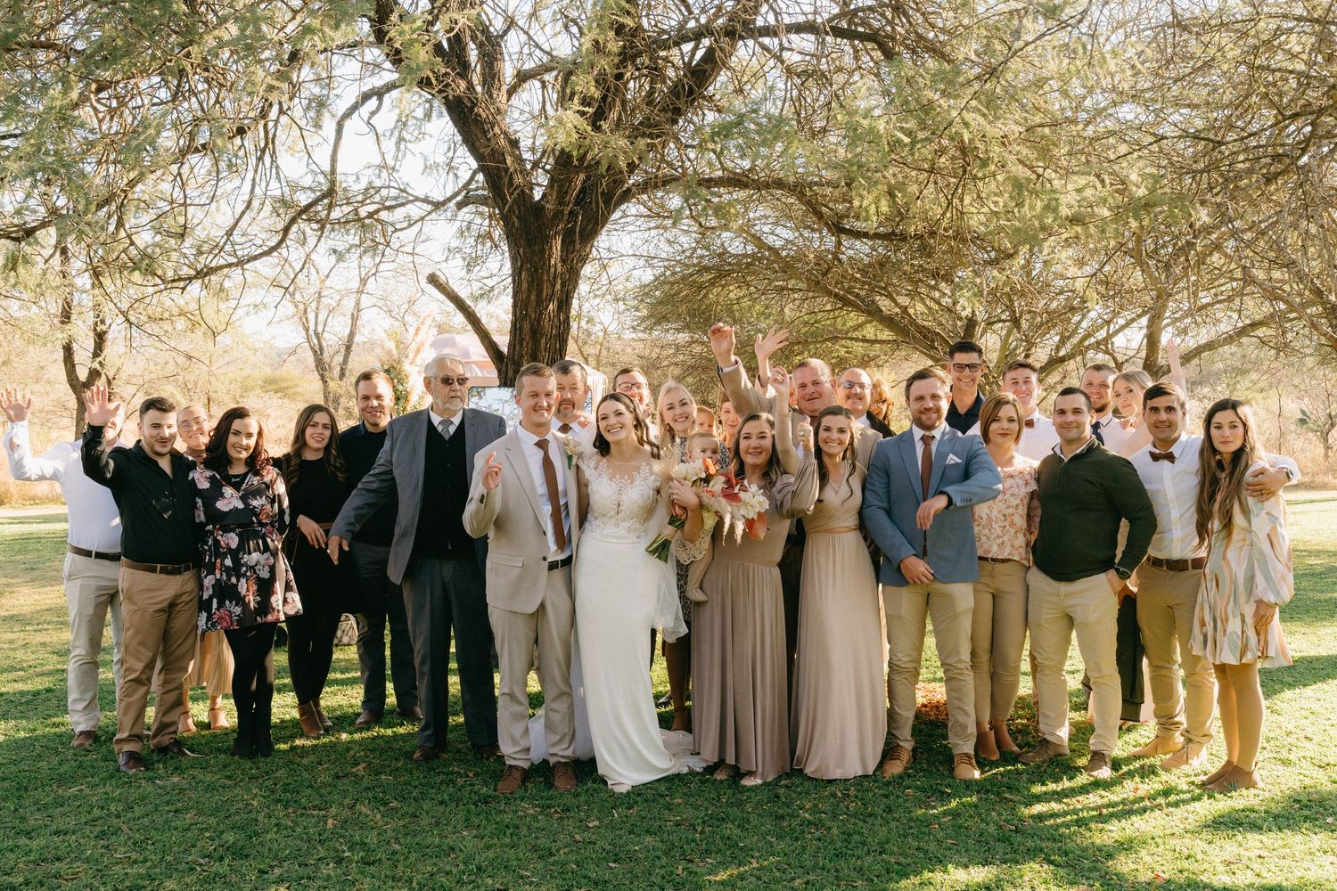 Wedding party gathered under blooming trees for outdoor group photos in neutral tones.