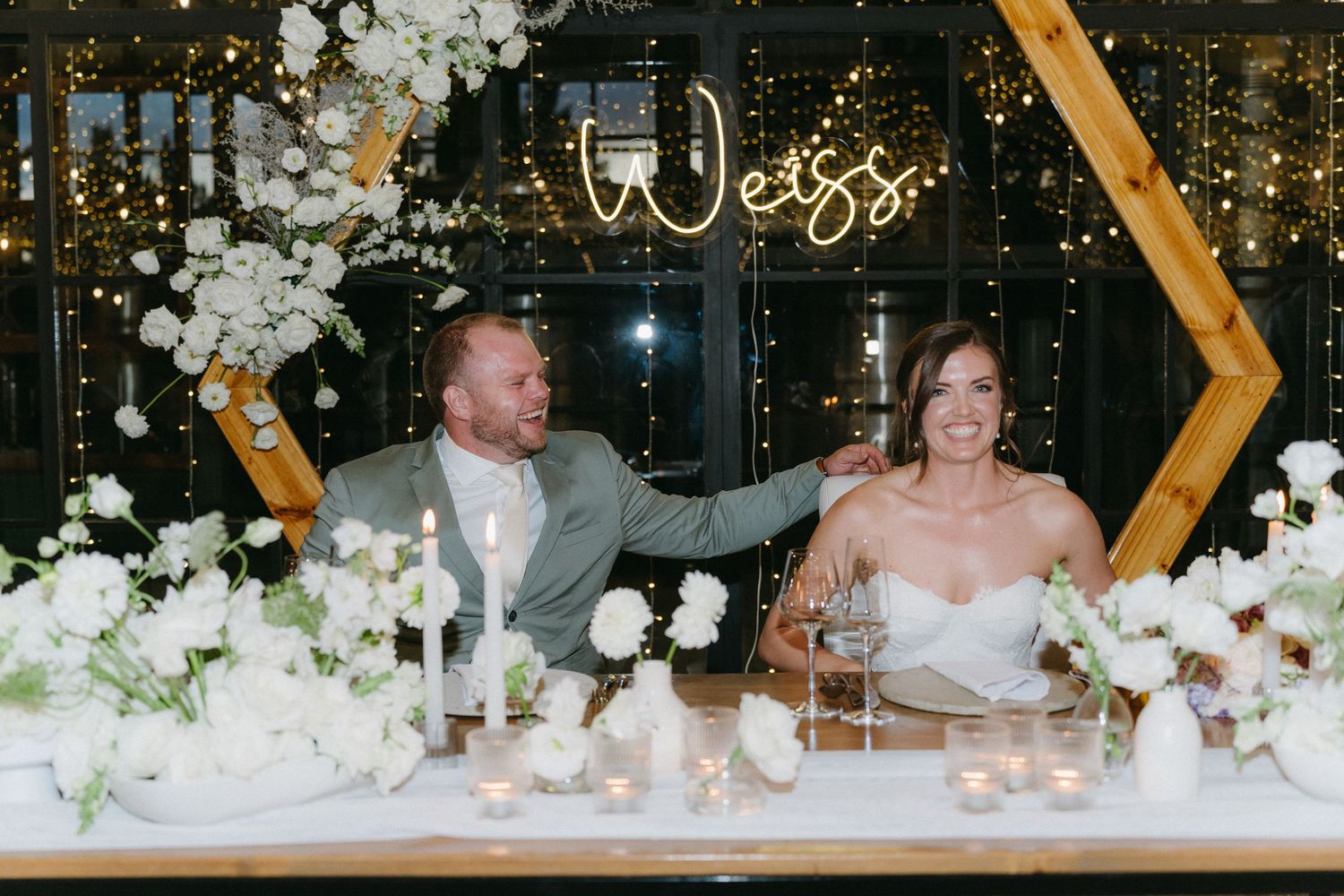 Wedding reception table decorated with white florals and illuminated welcome sign.