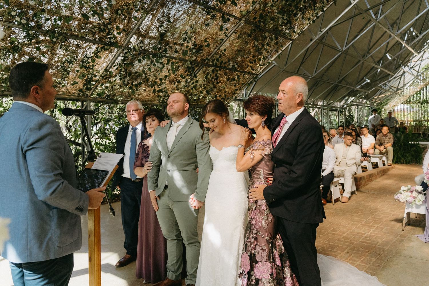 Wedding ceremony taking place inside a greenhouse venue with guests gathered around during an intimate celebration.