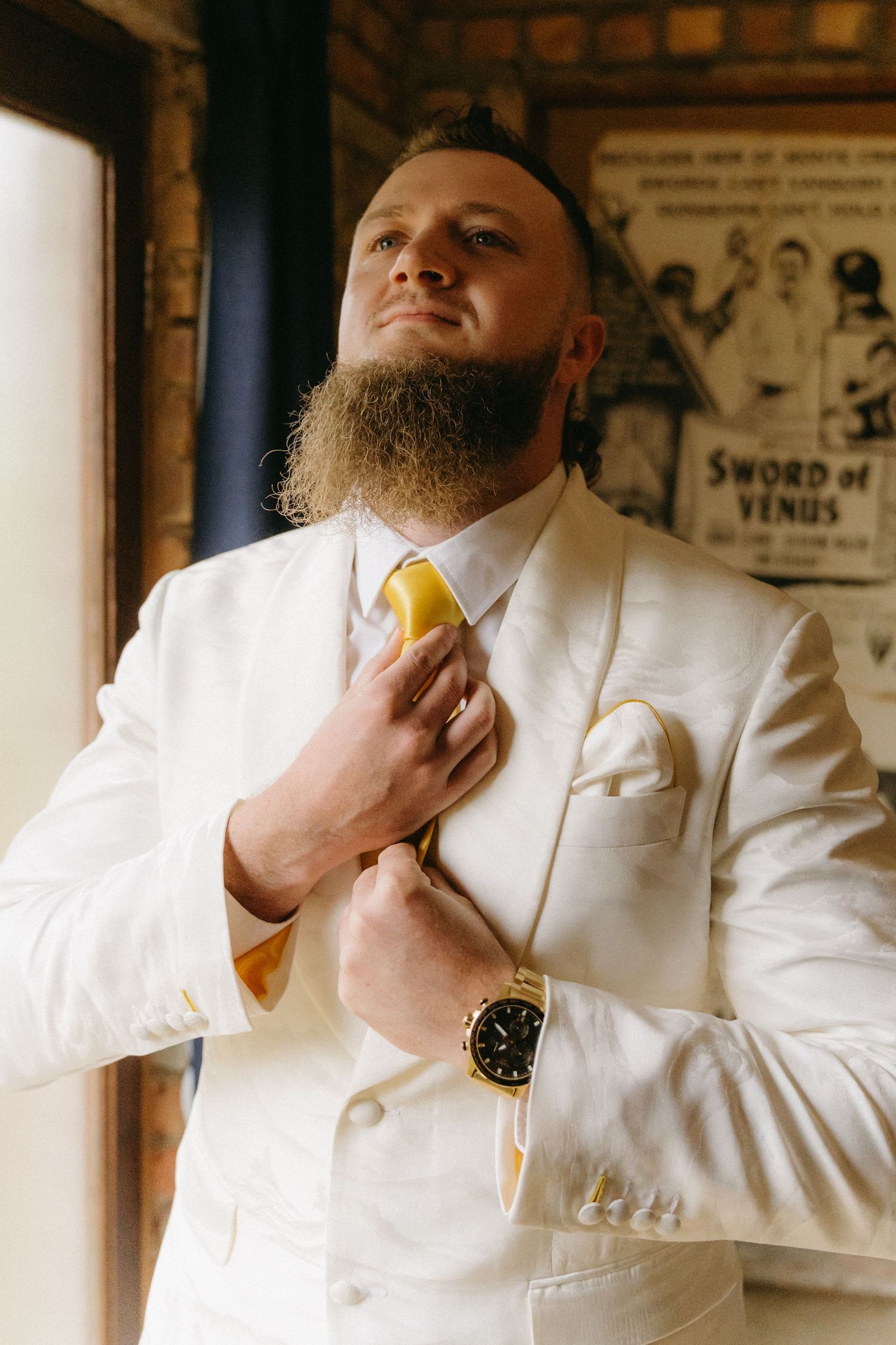 A well-dressed person in a crisp white suit and yellow tie adjusts their collar while wearing a watch.