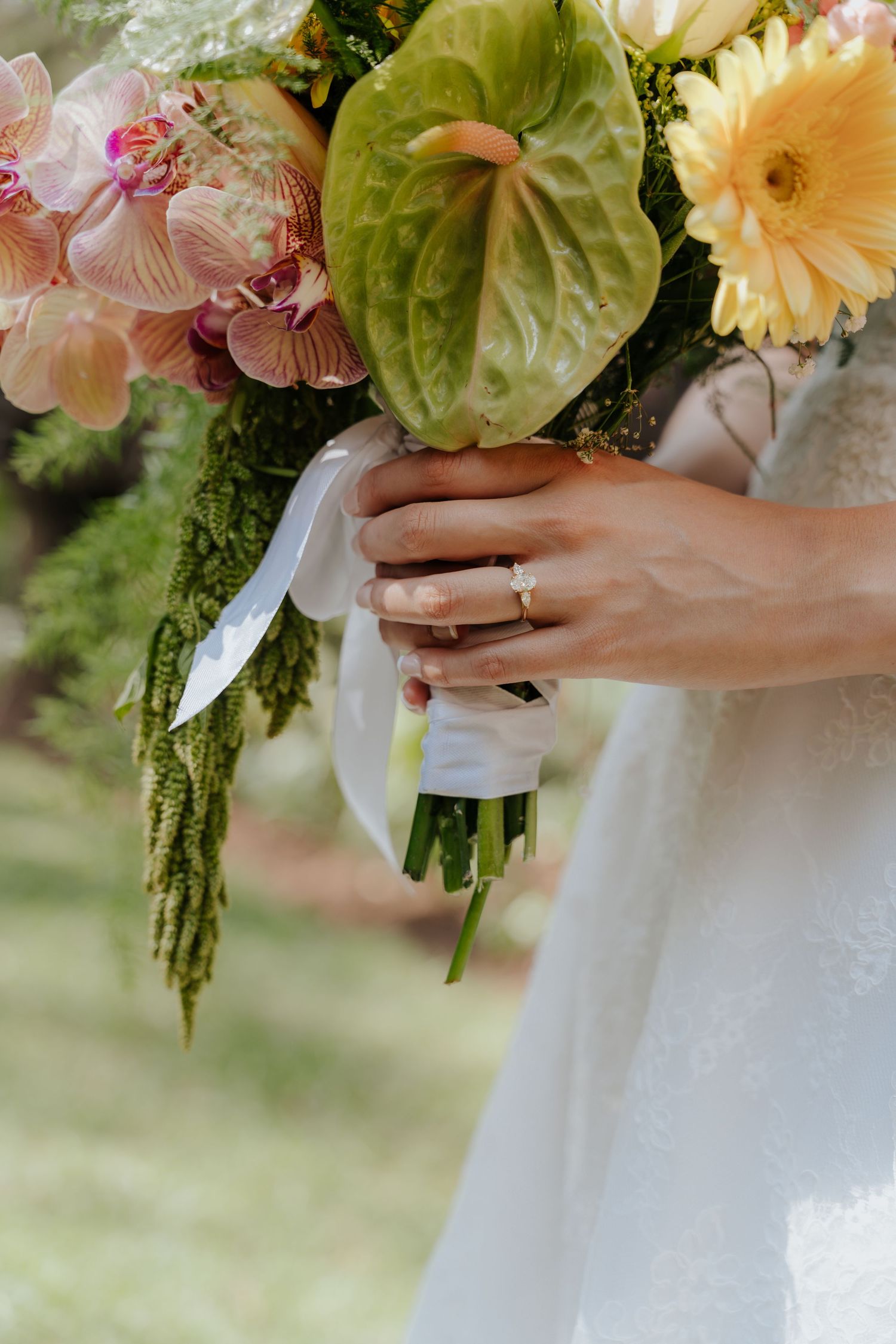A bridal bouquet of pale pink and white flowers with green foliage is held against a white wedding dress.
