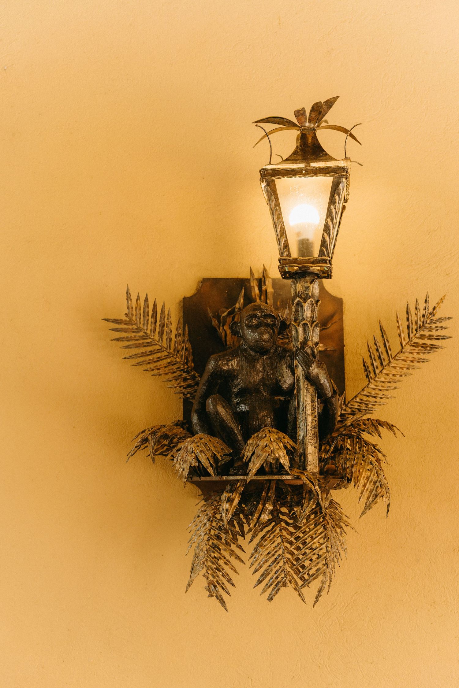 A vintage wall sconce with an ornate lantern light fixture surrounded by decorative metal ferns on a warm beige wall.