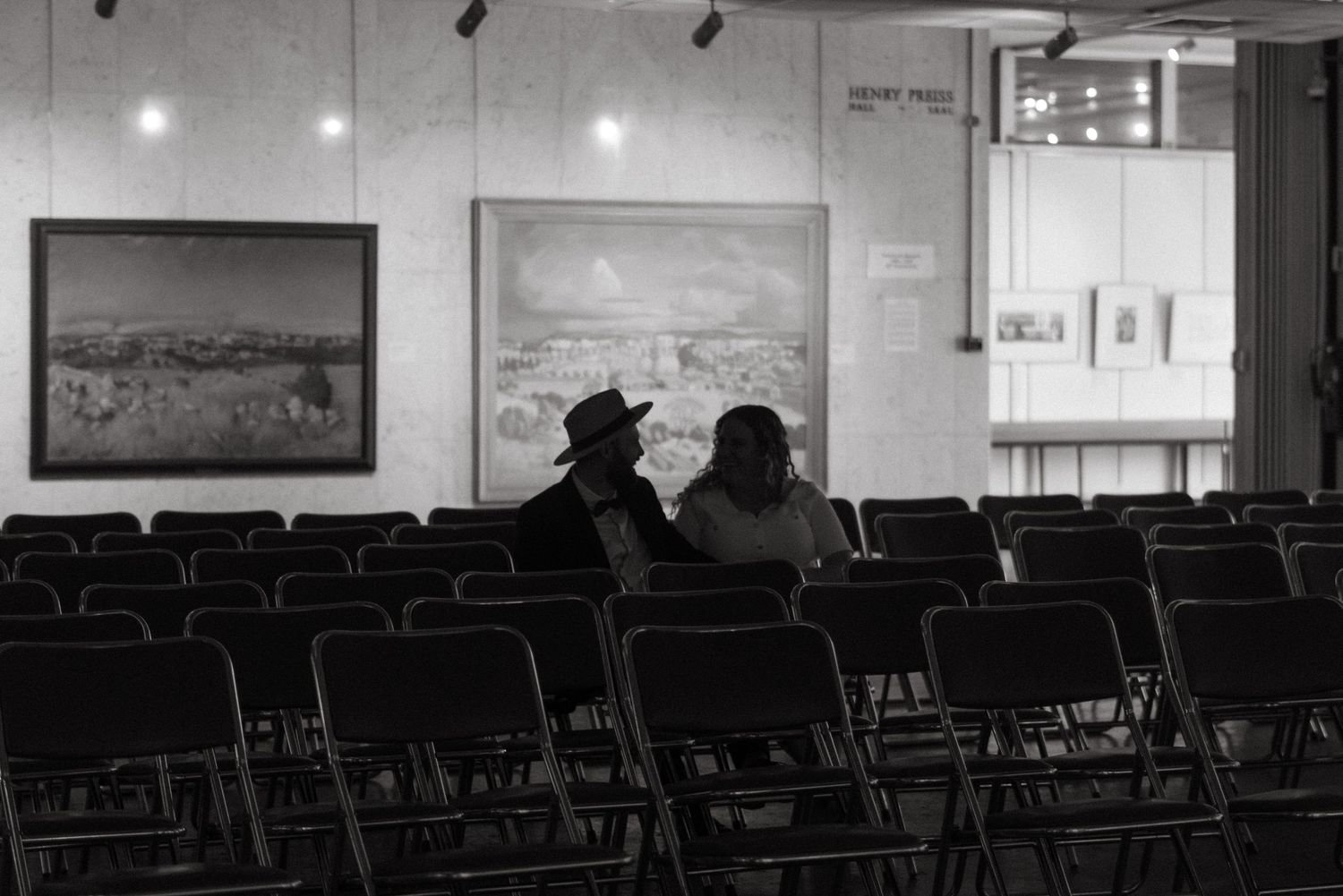 Black and white photo of two people sitting in empty auditorium looking at artwork.