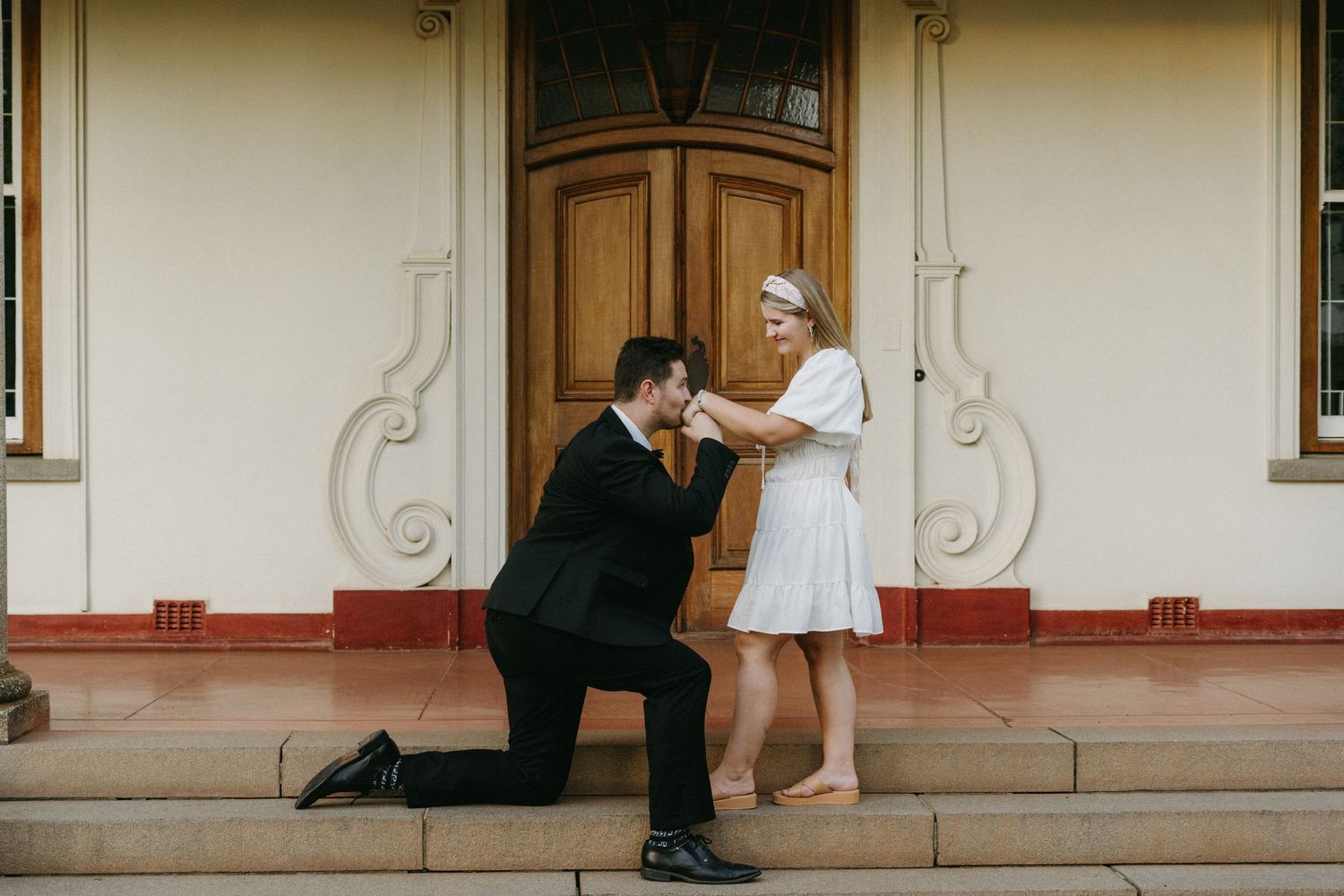 A romantic moment unfolds on the steps of a vintage building with ornate doors and architectural details.