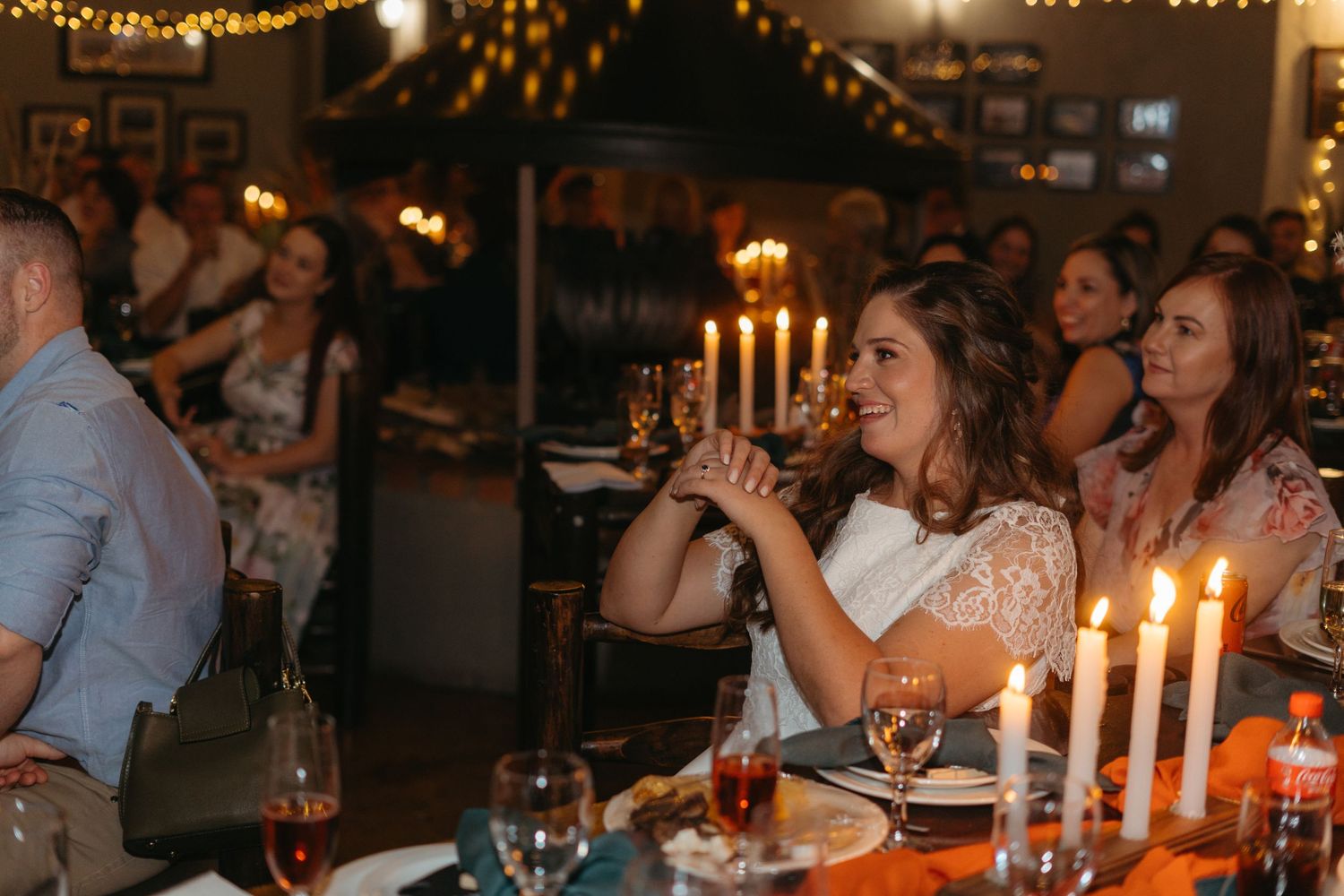 Wedding guests enjoying drinks and laughter at a candlelit reception dinner.