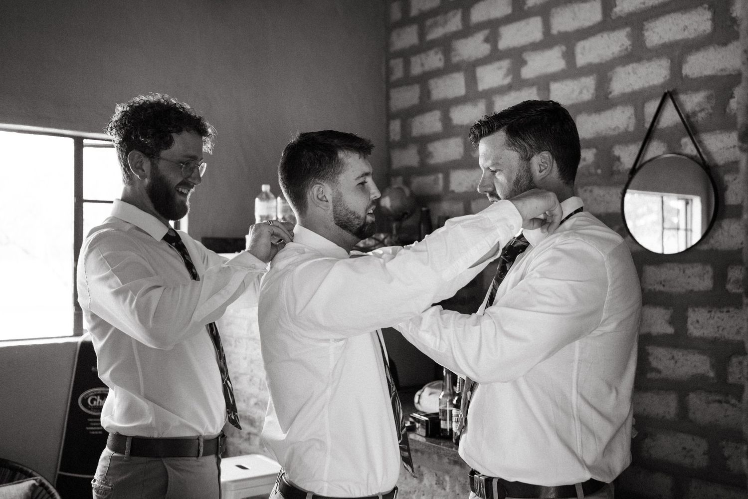 Groomsmen in white shirts helping each other adjust ties and get ready for wedding day.