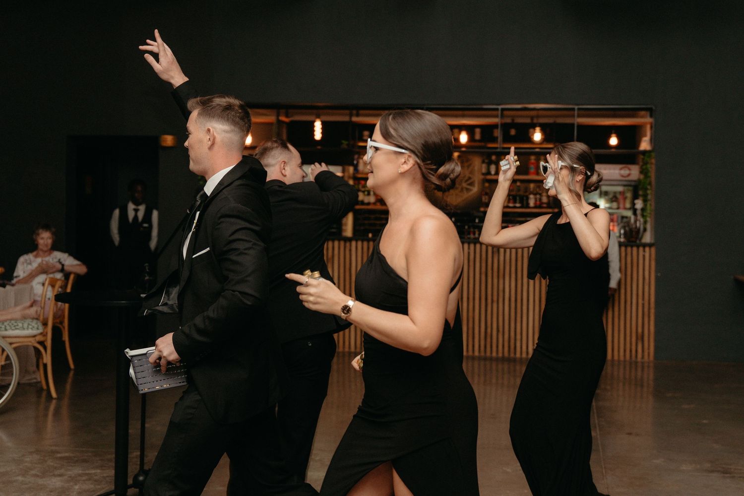 A group of people dance together in formal attire at a dimly lit event venue.