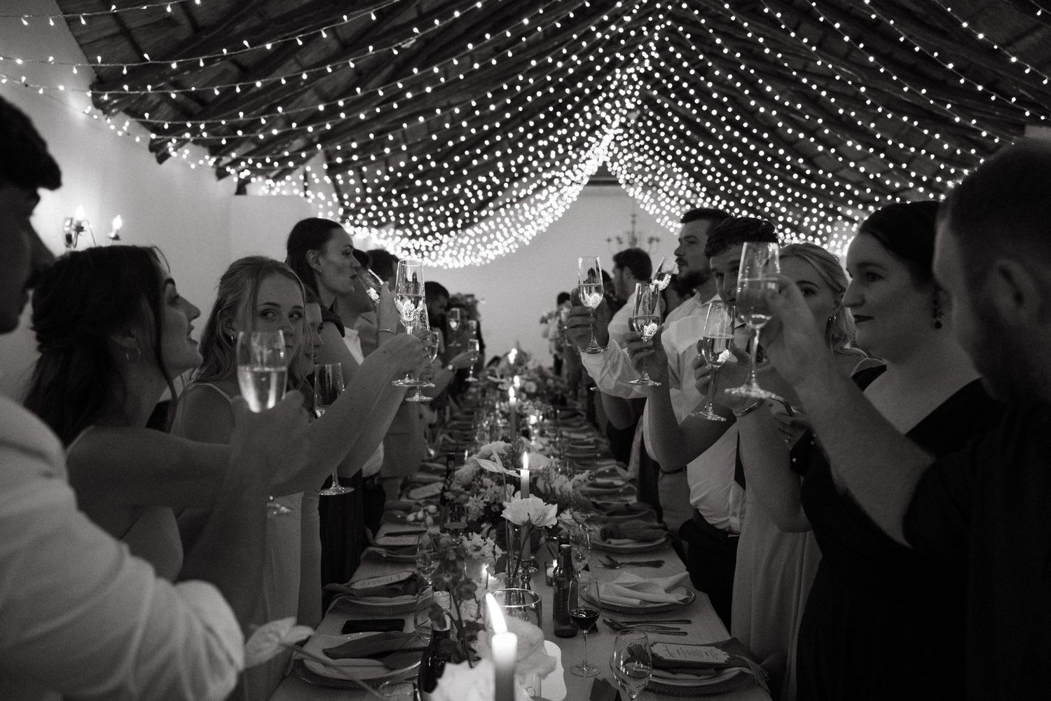 Wedding guests dance under a canopy of twinkling string lights during an evening reception celebration.