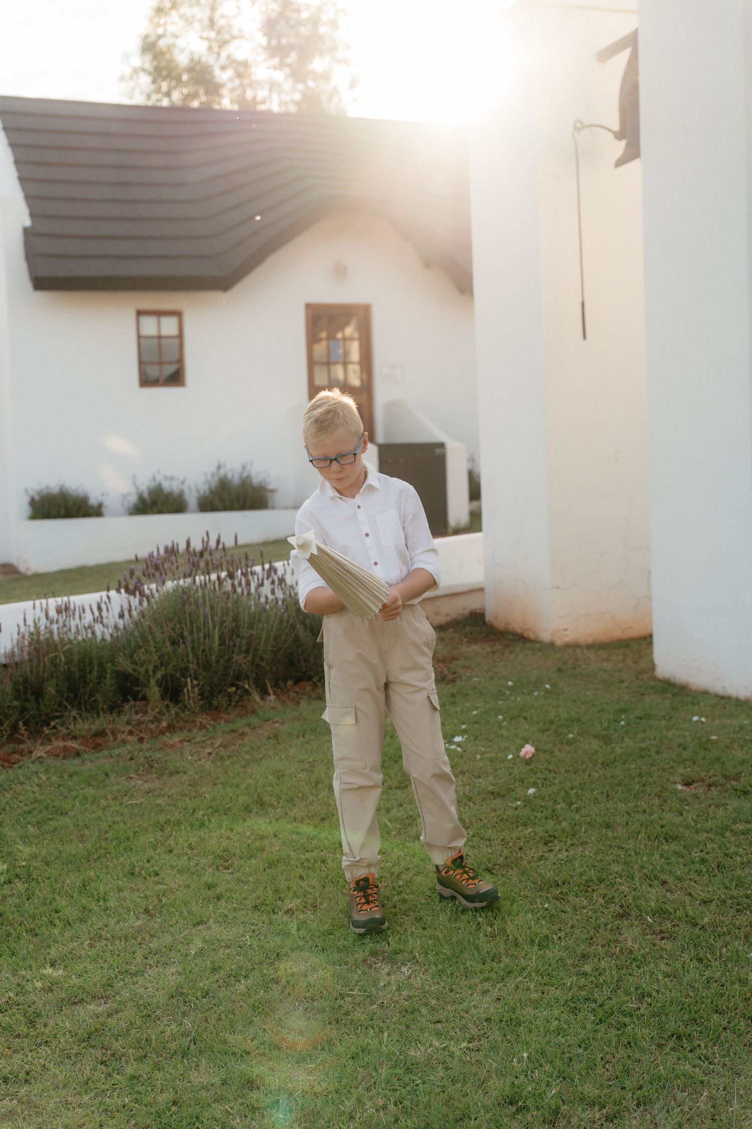 A person in white clothing bends down to examine something on a grassy lawn near a white building.
