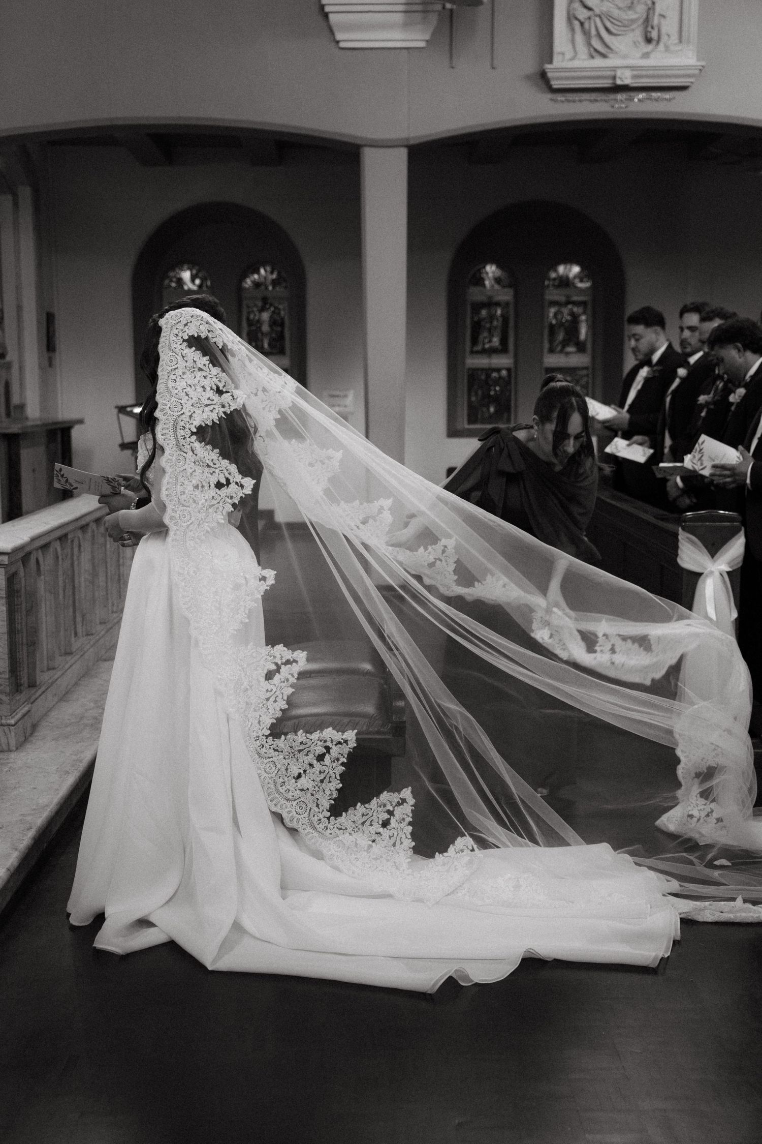 Black and white image of bride in cathedral lace veil kneeling during wedding ceremony at Rosebank Catholic Church in Johannesburg